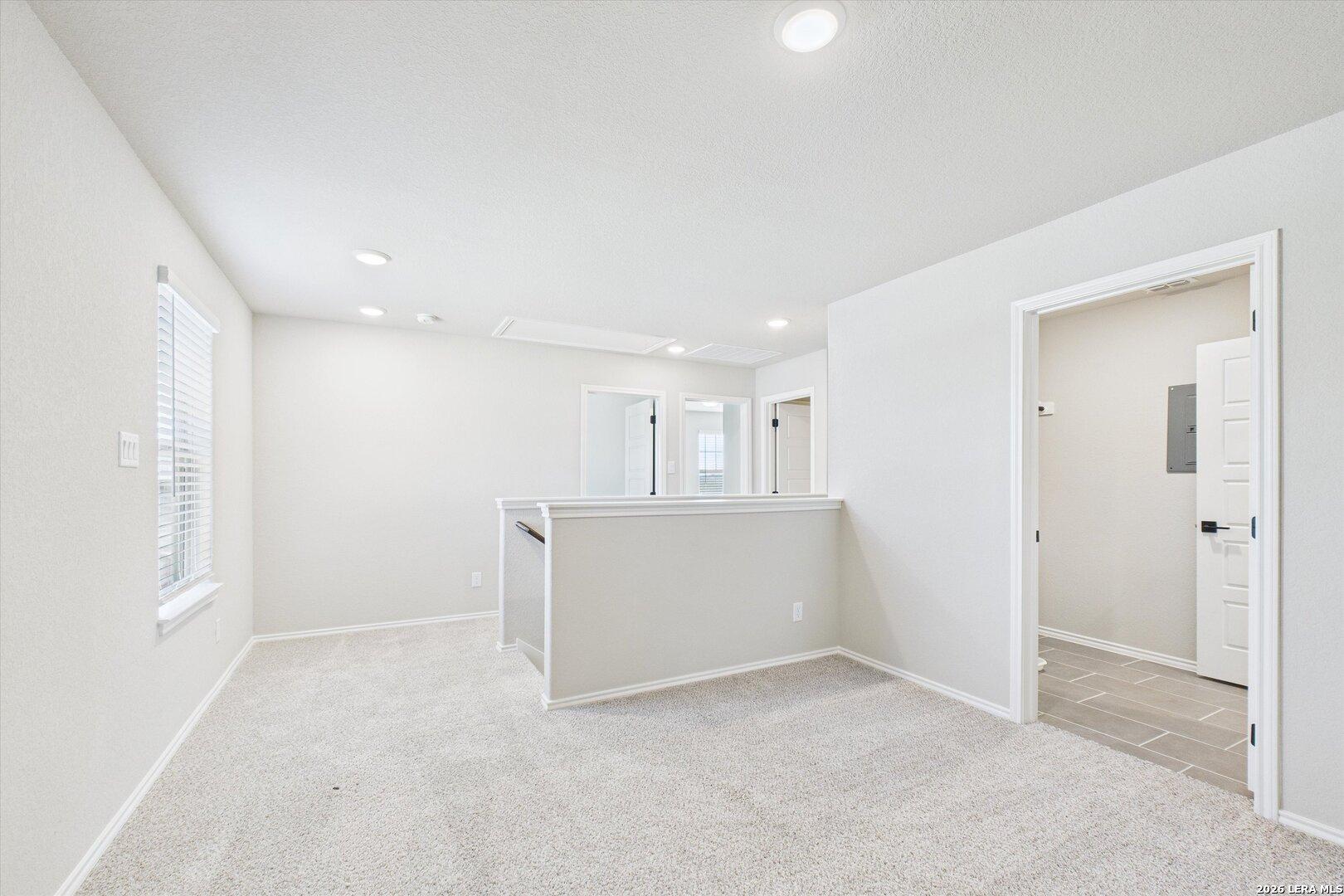 Bright upstairs hallway with white walls, beige carpet, recessed lights, and bedroom doors in Davidson Homes Charlotte A, San Antonio