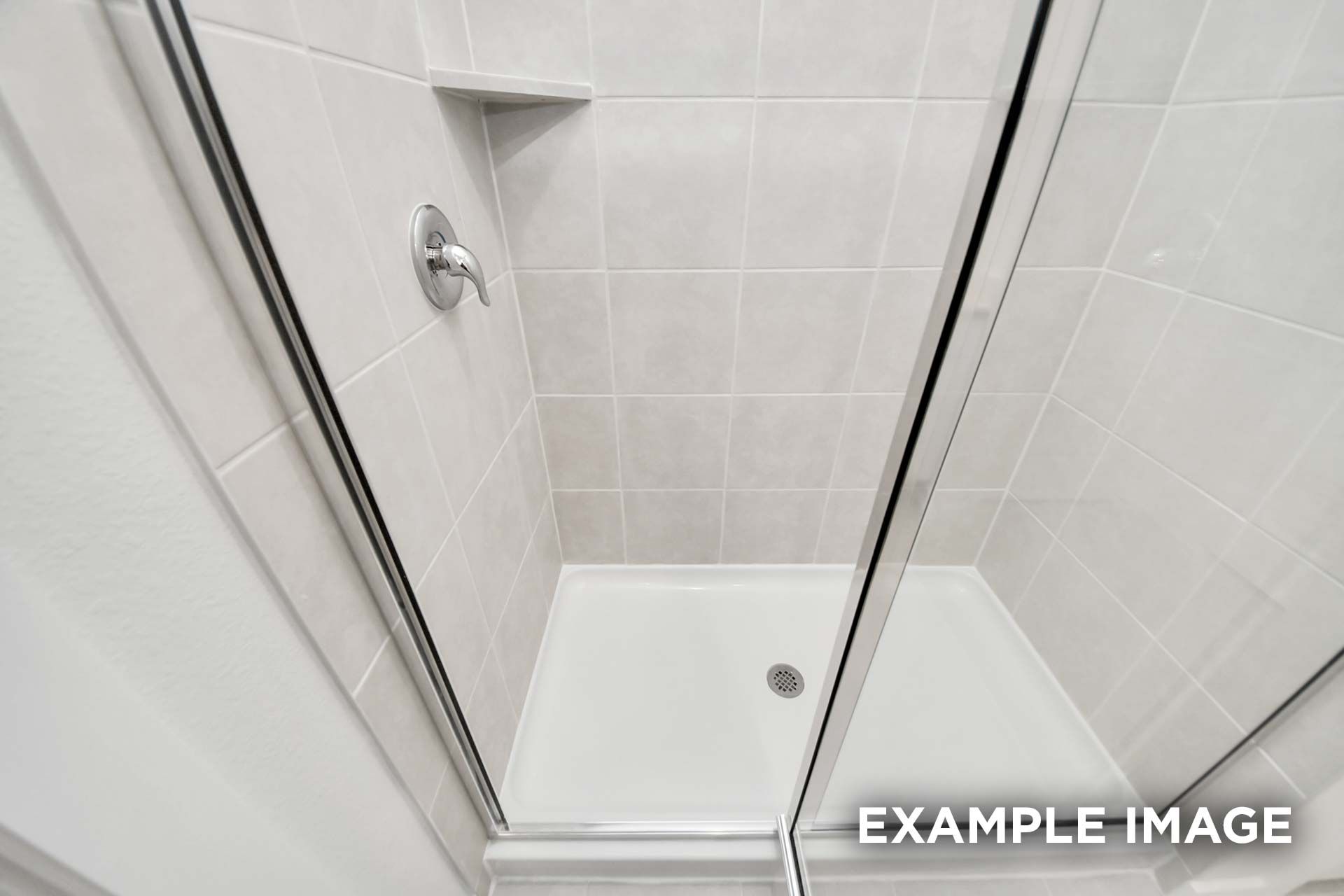 White tiled walk-in shower with sliding glass doors and built-in shelf in The Blanco master bathroom by Davidson Homes