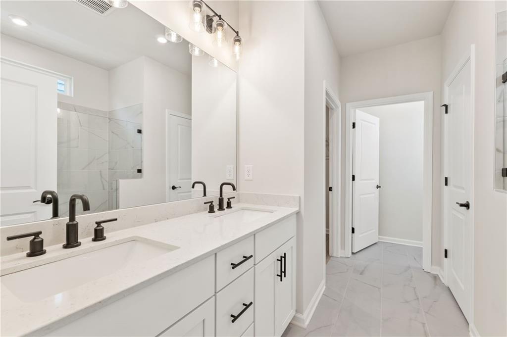 Modern master bathroom featuring double vanity with black faucets, glass shower, and white cabinetry in Davidson Homes The Daphne C, Loganville, GA