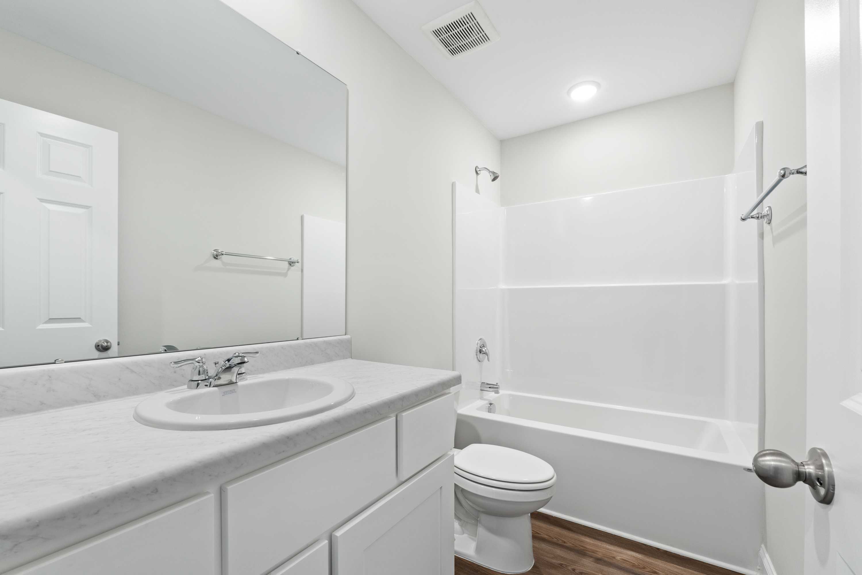 Spacious bathroom in Chapel Hill Athens AL with white vanity, mirror, bathtub shower combo, toilet and hardwood floors by Davidson Homes