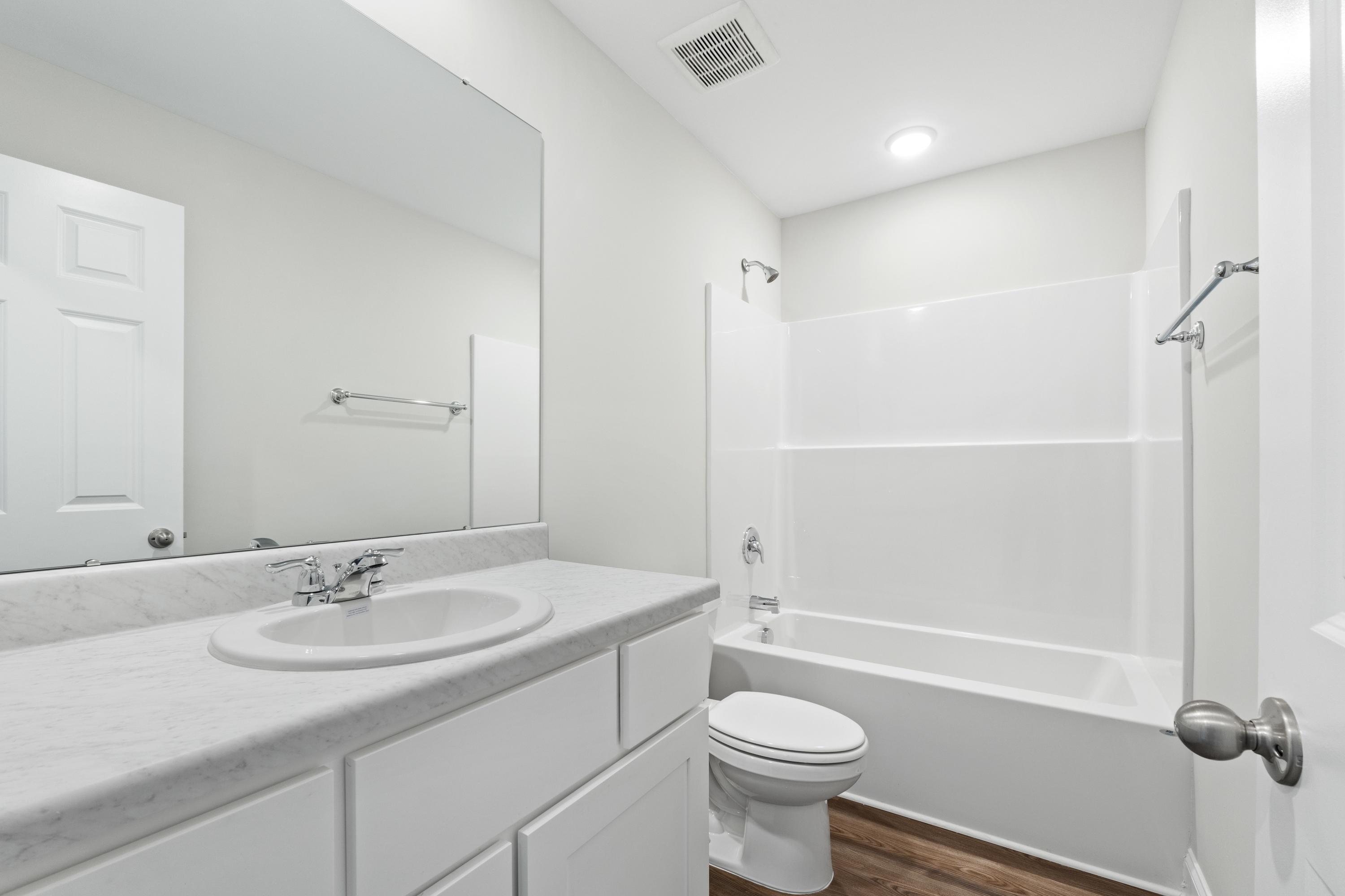 Spacious bathroom in Chapel Hill Athens AL with white vanity, mirror, bathtub shower combo, toilet and hardwood floors by Davidson Homes