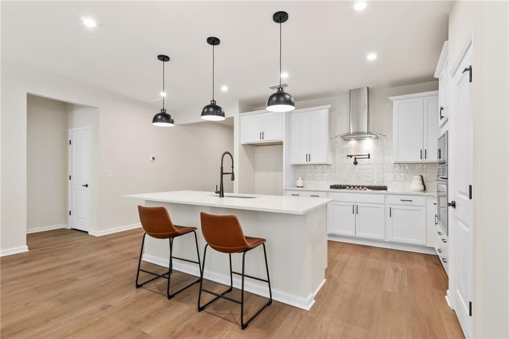 Modern white kitchen island with farmhouse sink, pendant lights, and stainless appliances in Davidson Homes The Daphne B, Loganville, GA