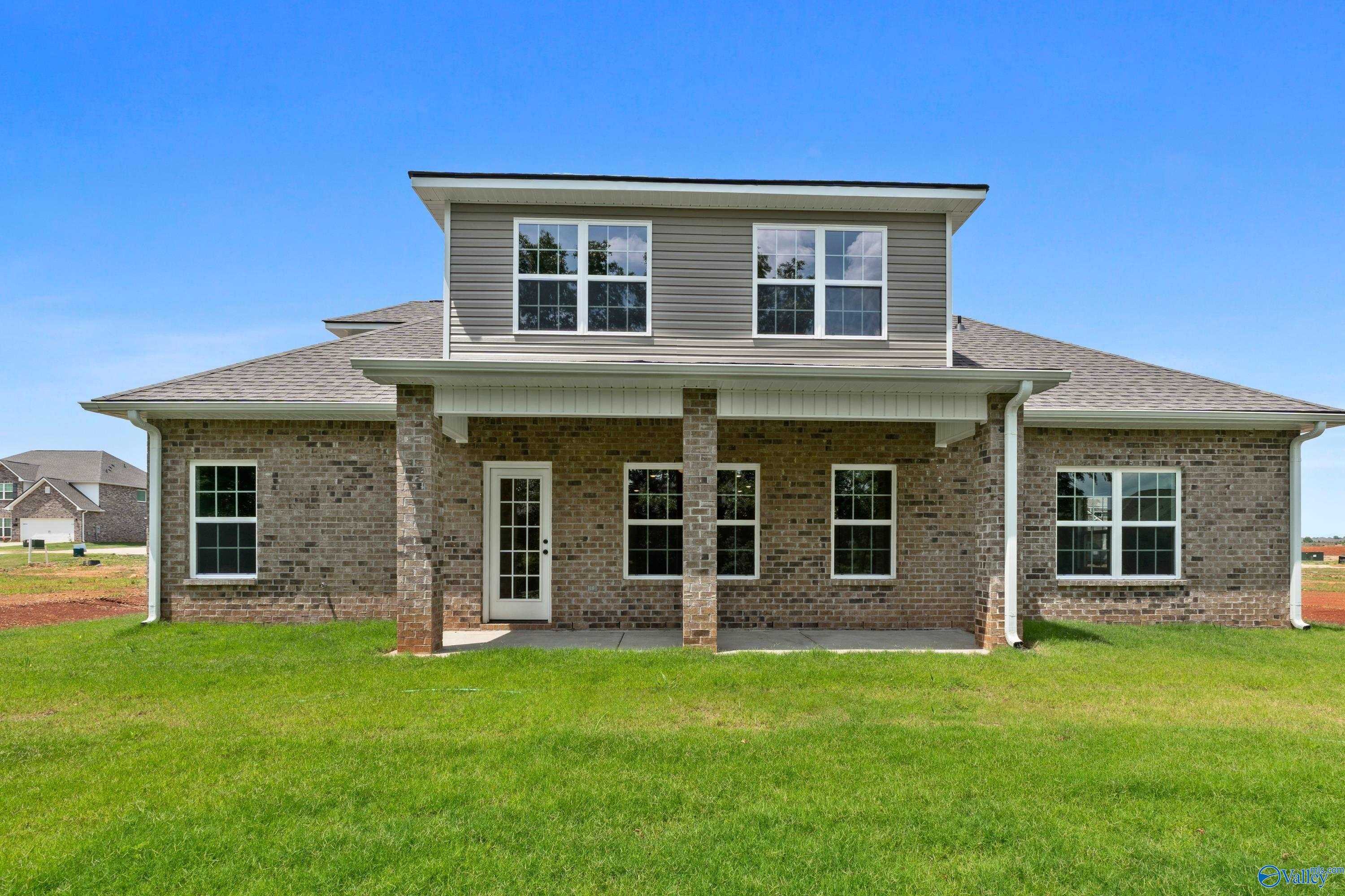 Brick home exterior with covered patio, large windows, and lush green lawn in Creekside, Harvest, Alabama