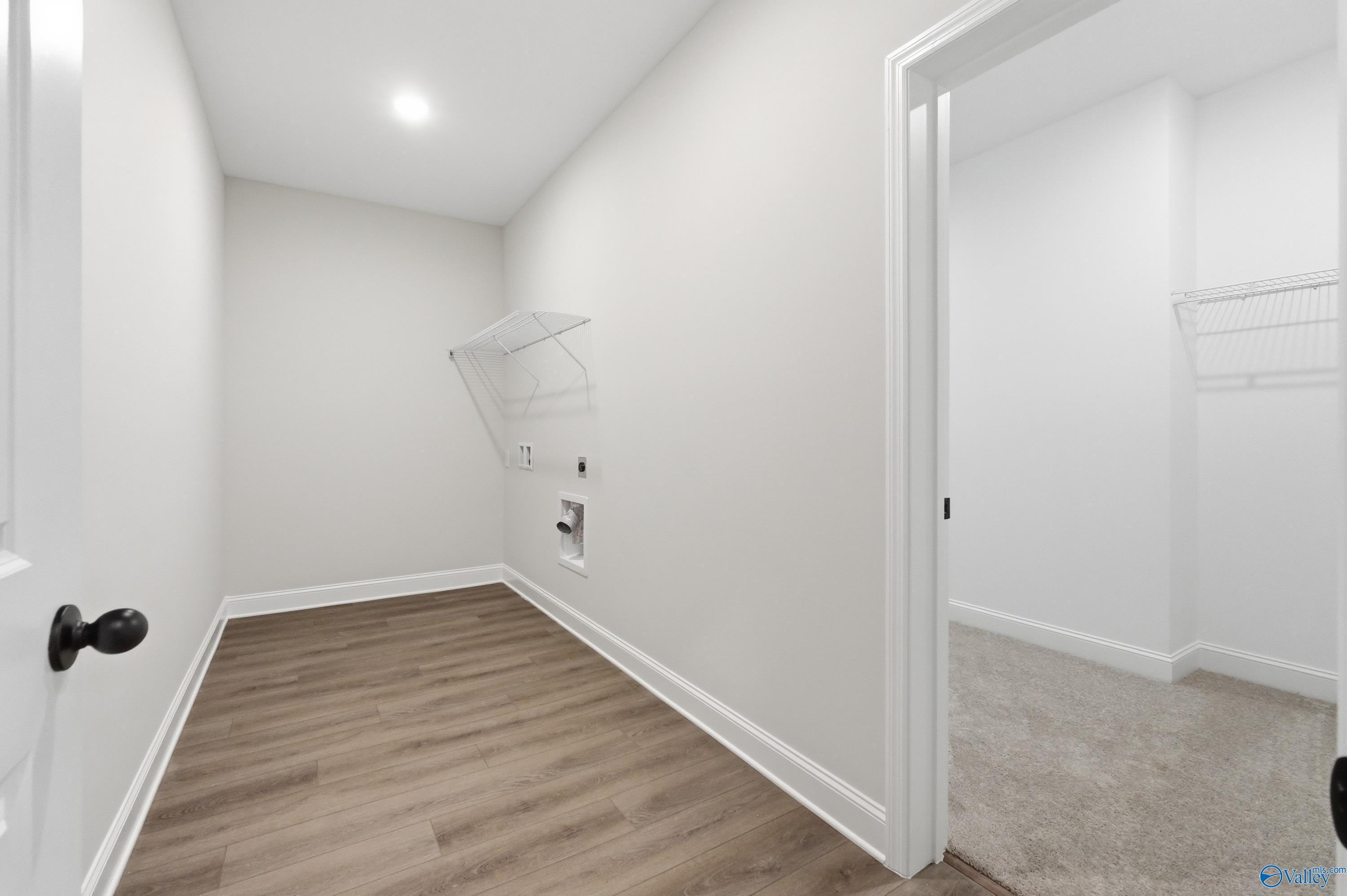 Spacious laundry room featuring white walls, LVP flooring, wire shelving, and hookups in Davidson Homes The Rockford B, Athens, Alabama