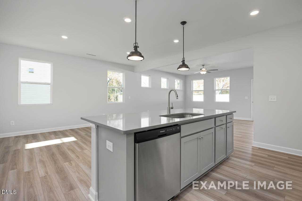 Modern open-concept kitchen with gray island, stainless dishwasher, sink, and pendant lights in The Adalynn A, Lillington, NC