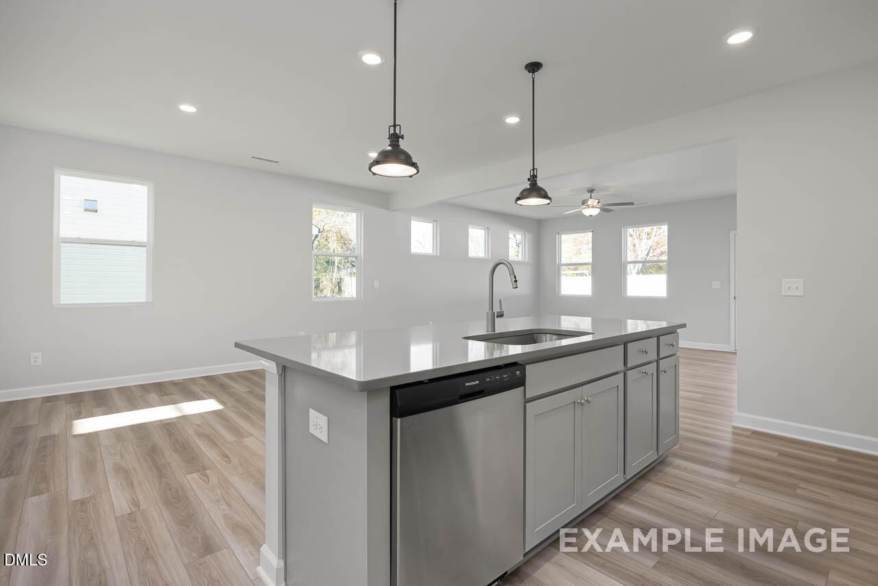 Modern open-concept kitchen with white cabinets, quartz island sink, stainless dishwasher, and pendant lights in The Adalynn A, Lillington, NC