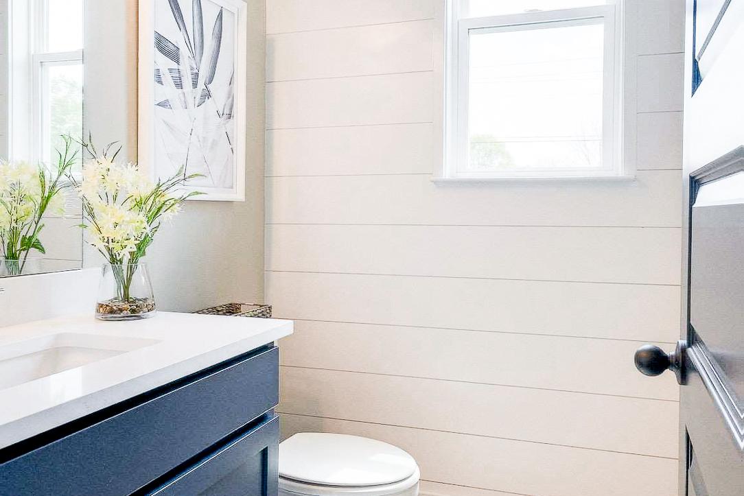 Cozy bathroom at The Meadows in Smyrna TN featuring white shiplap walls, navy vanity, plaid window valance, and natural light
