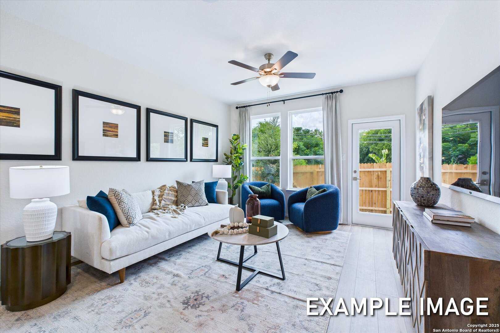 Bright modern living room with white sofa, blue velvet chairs, ceiling fan, and sliding doors to backyard in The Gillian C, San Antonio, Texas