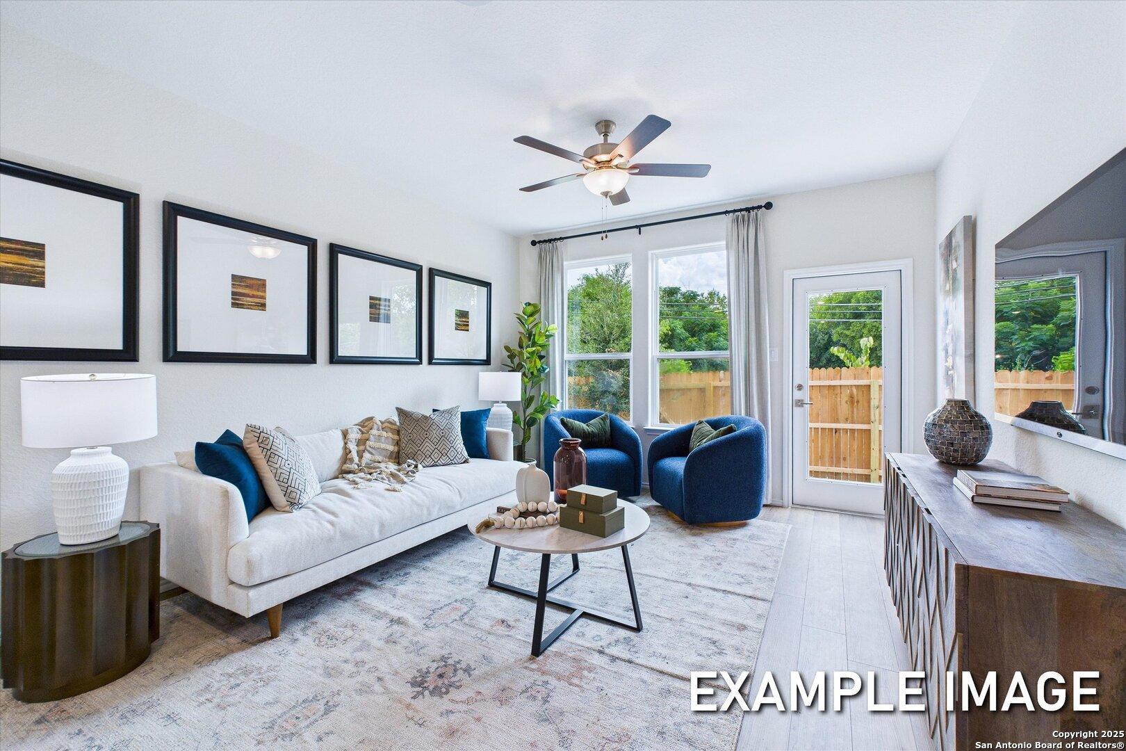 Cozy modern living room with white sofa, blue velvet chairs, large windows, ceiling fan in Davidson Homes The Gillian C, San Antonio