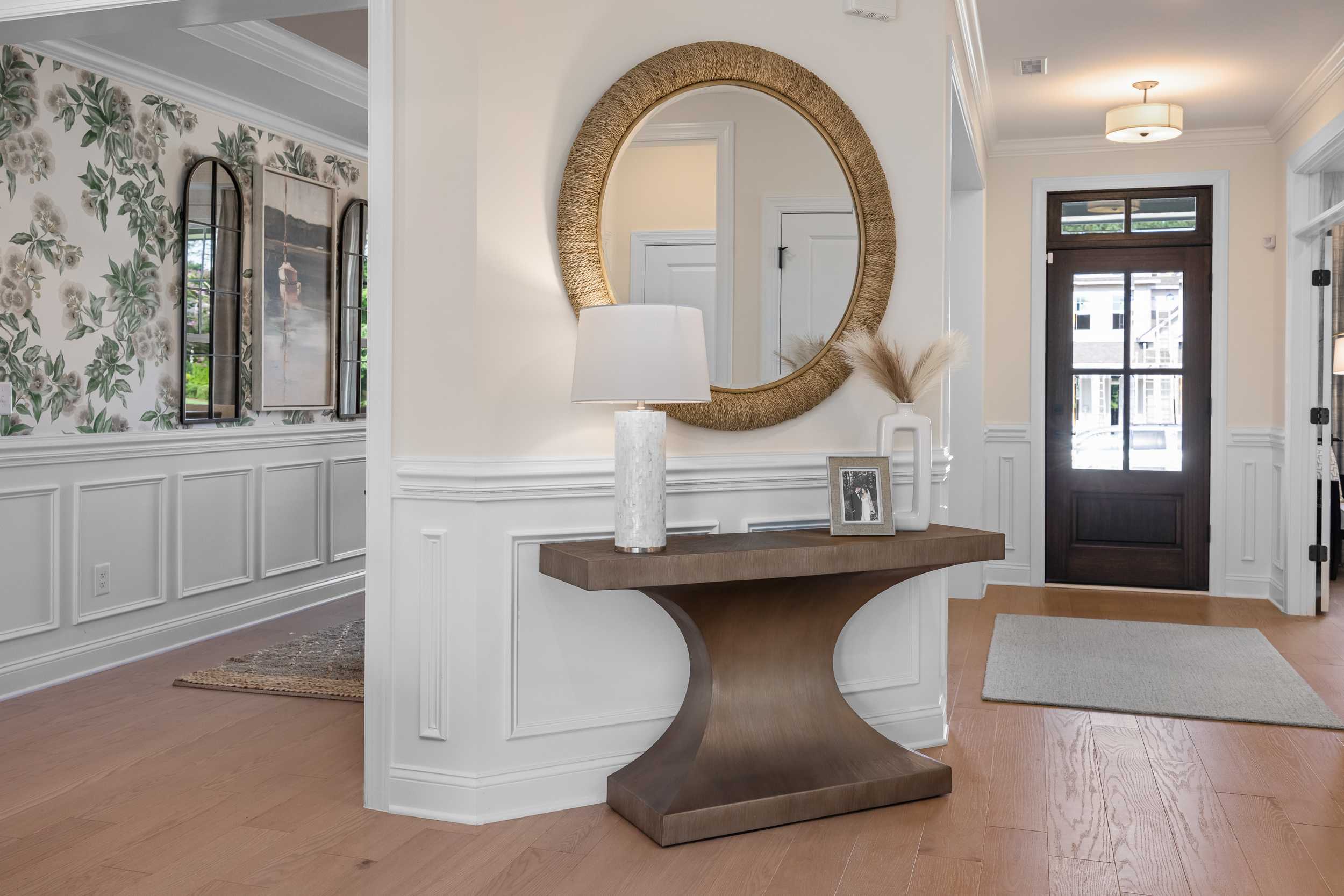 Elegant entryway at Laneridge Estates in Raleigh NC with round gold mirror, console table, floral wallpaper and hardwood floors