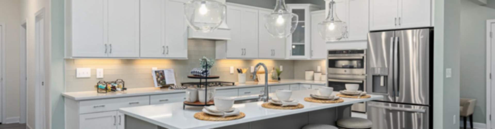 Modern kitchen in new Fayetteville home with white cabinets, gray island, bar stools, stainless steel appliances, pendant lights
