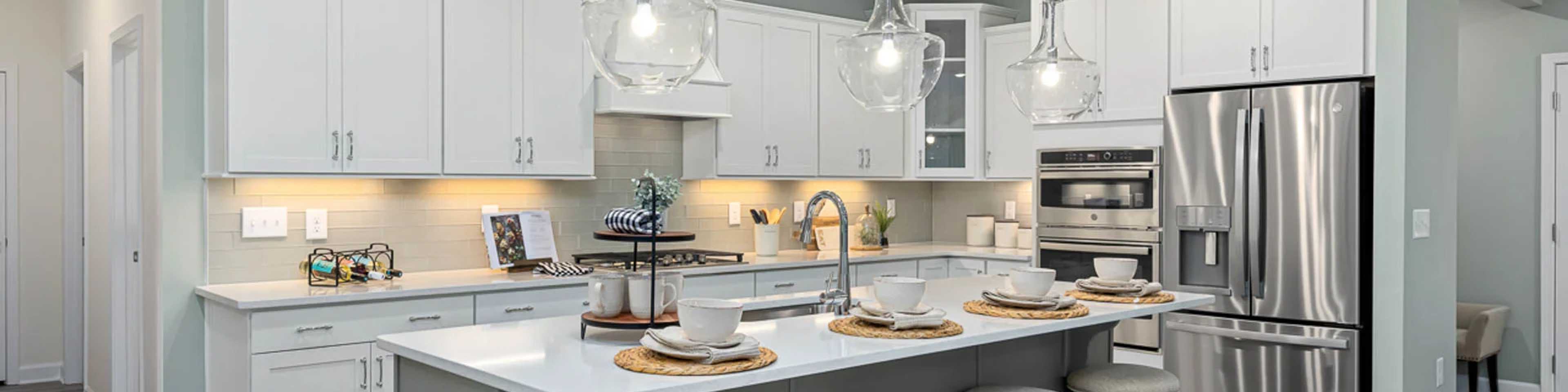 Modern kitchen in new Fayetteville home with white cabinets, gray island, bar stools, stainless steel appliances, pendant lights