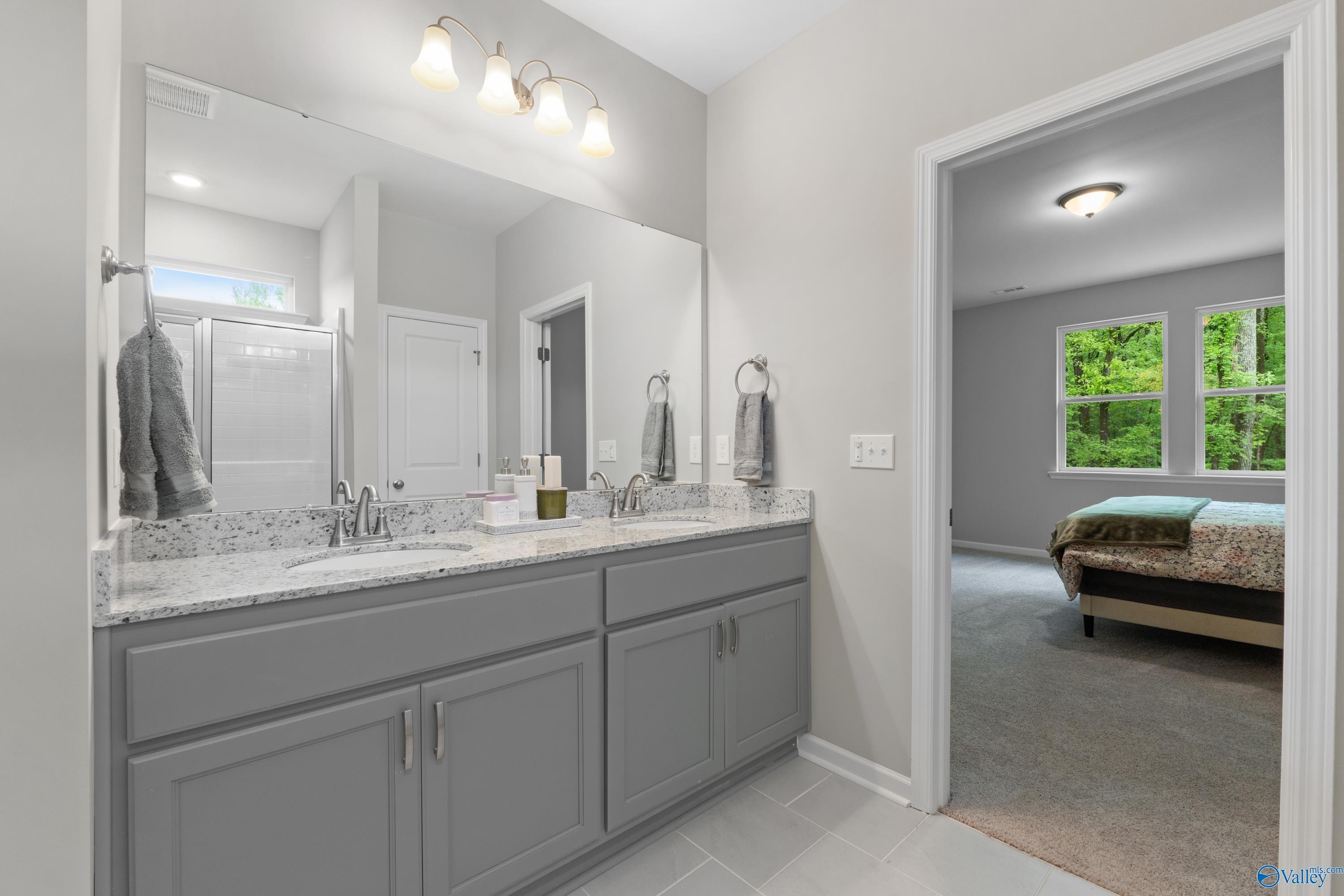 Modern master bathroom with double gray vanity, quartz counters, and adjacent bedroom view in Davidson Homes The Luna, Hazel Green, Alabama