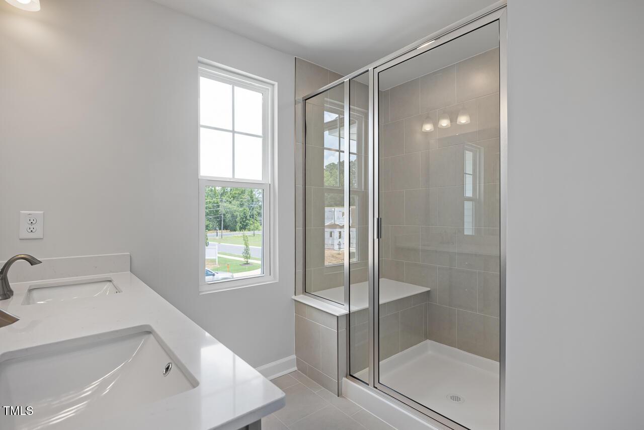 Modern master bathroom with frameless glass shower, white quartz vanity, and window overlooking greenery in Davidson Homes The Warren, Fuquay-Varina, NC