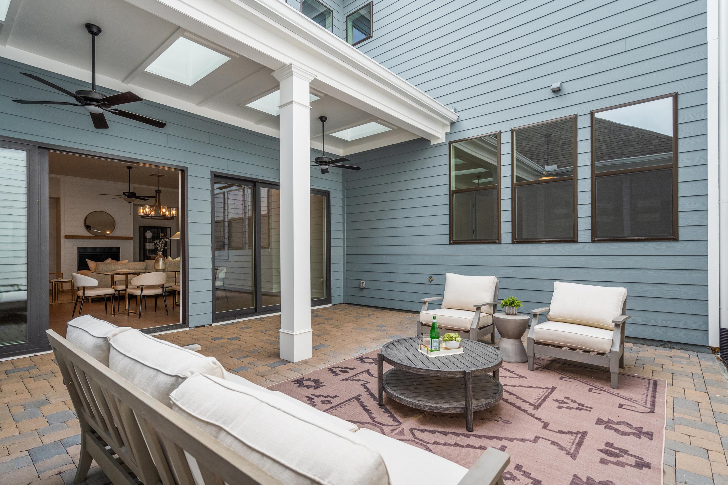 Covered patio with white cushioned seating at The Village at Towne Lake in Woodstock GA, blue exterior, ceiling fans, sliding doors to fireplace room