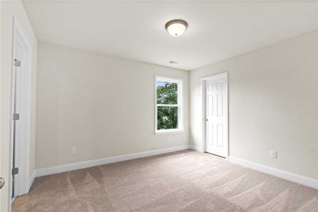 Bright secondary bedroom with beige walls, plush carpet, window view of trees in Davidson Homes The Hickory B at Wehunt Meadows, Hoschton