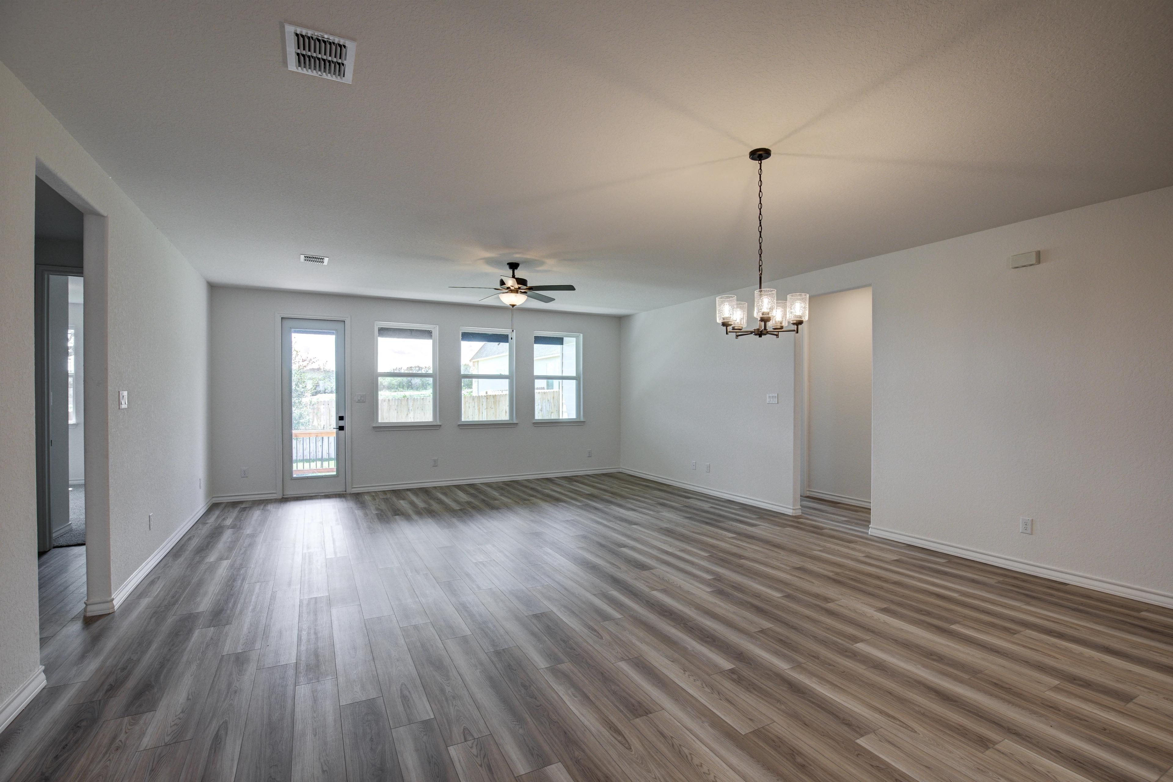 Spacious open-concept living room in The Lanier by Davidson Homes with hardwood floors, large windows, ceiling fan, and chandelier