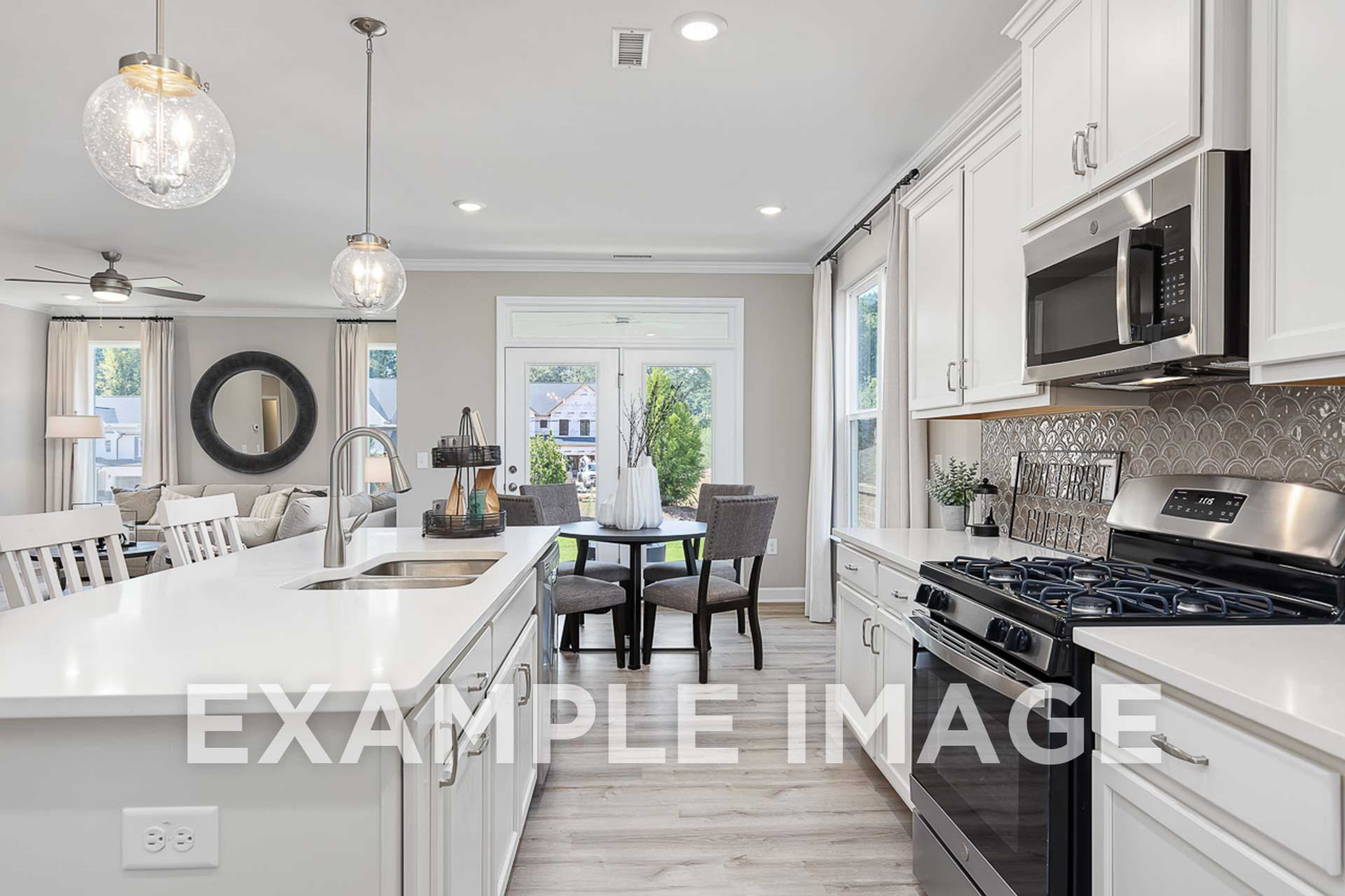 Spacious open-concept kitchen in The Ash D showcasing white cabinets, quartz counters, stainless steel appliances, and dining nook