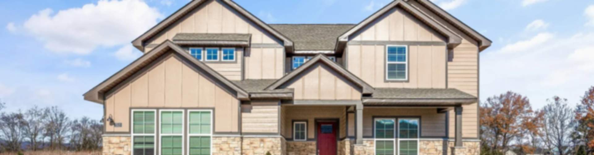 Modern two-story beige home with stone accents, red door, and porch in Cusseta new community