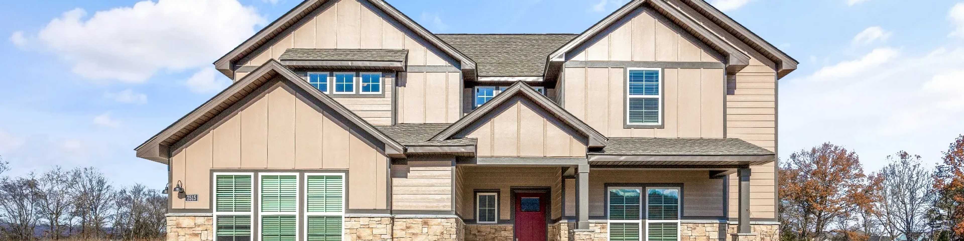 Modern two-story beige home with stone accents, red door, and porch in Cusseta new community