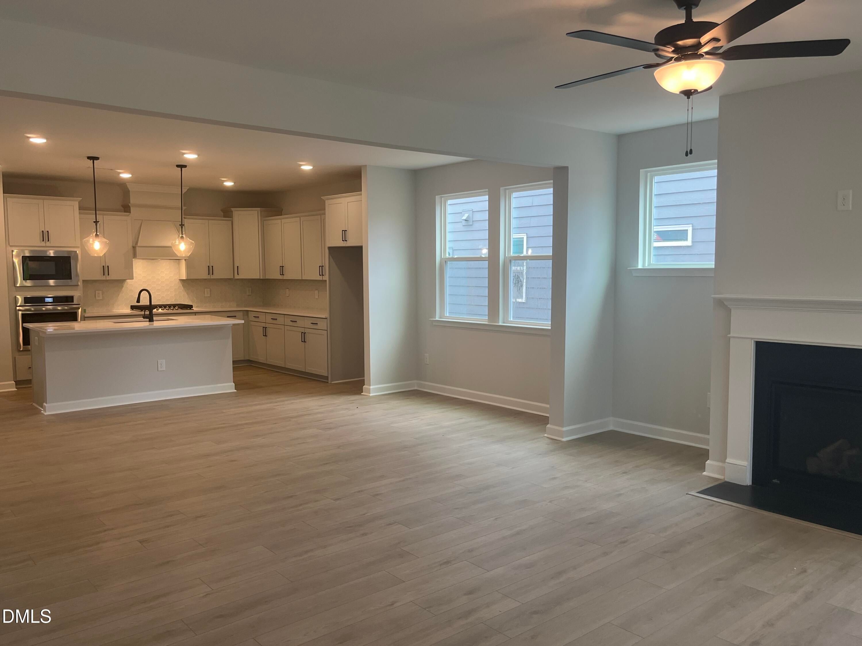 Open-concept kitchen with white cabinets, large island, stainless appliances, and adjacent living room featuring gas fireplace in Davidson Homes The Birch II E, Wake Forest NC