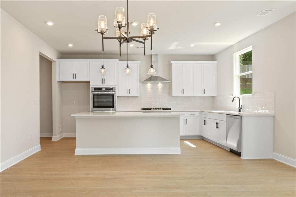 Modern white kitchen island with stainless steel appliances and chandelier in Davidson Homes The Hickory E, Buford, Georgia