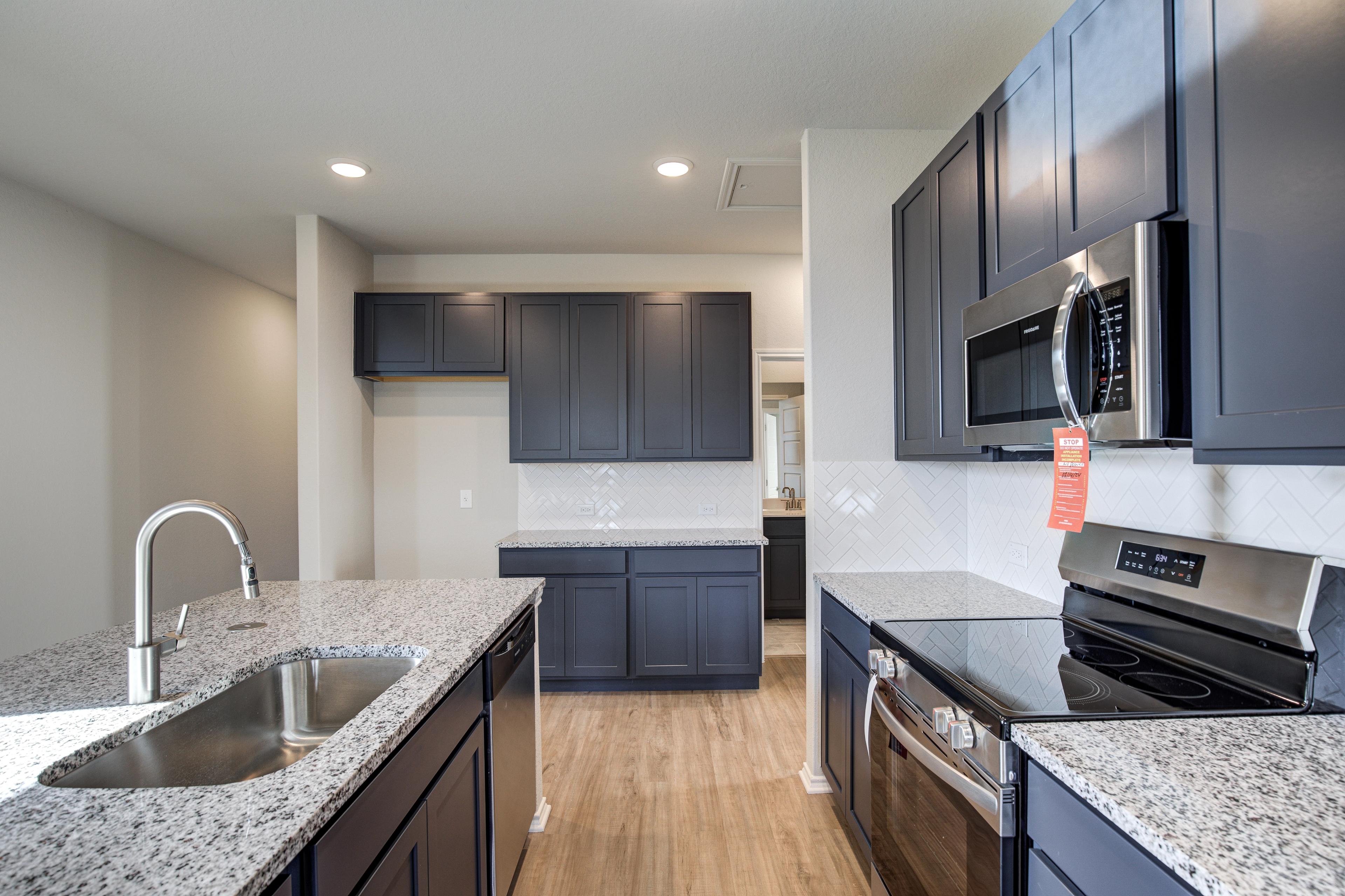 Modern kitchen in The Frio D by Davidson Homes with dark shaker cabinets, granite counters, subway tile backsplash, stainless appliances