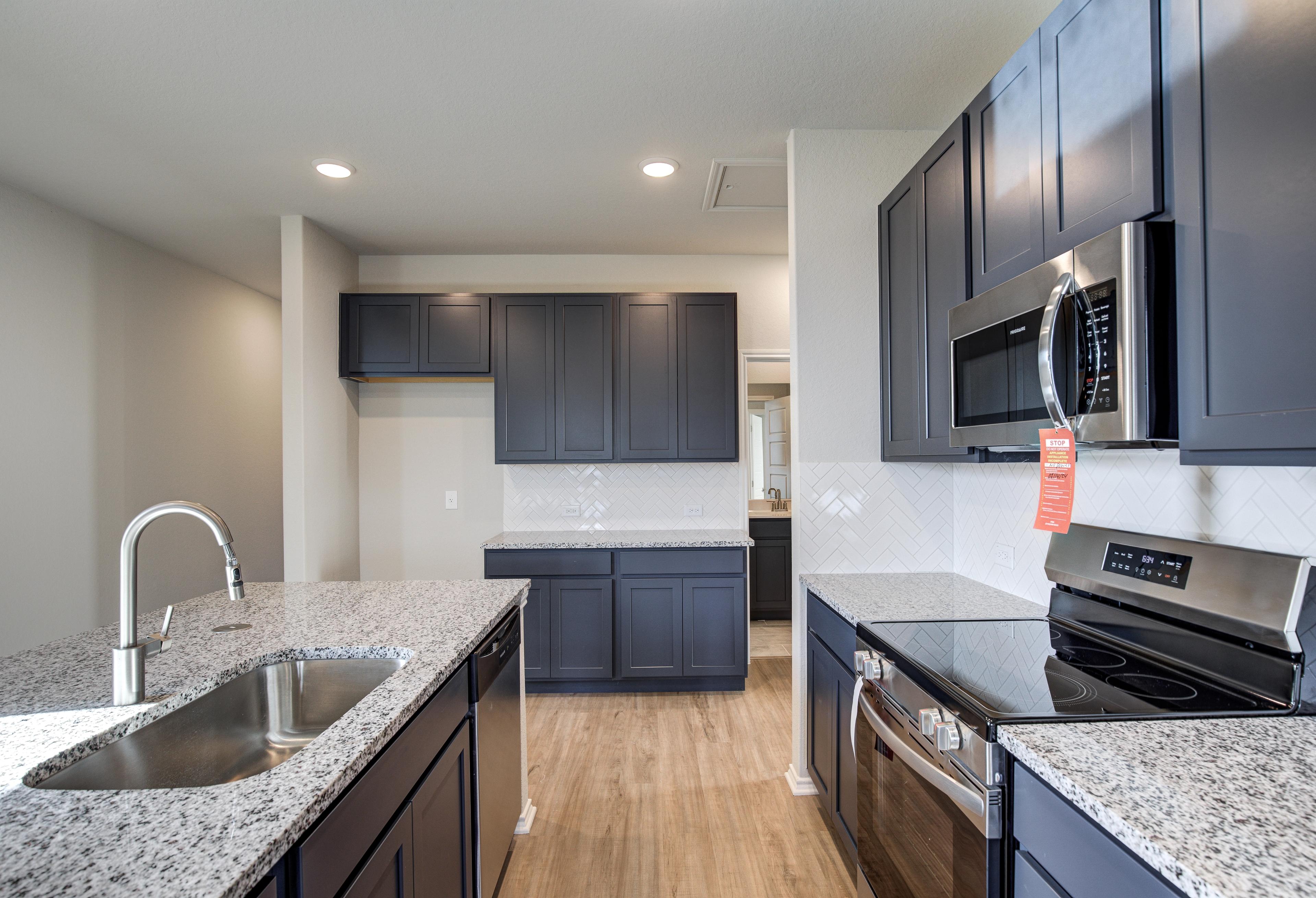 Spacious kitchen in The Frio C featuring navy cabinets, granite island with sink, stainless steel oven and microwave, subway tile backsplash