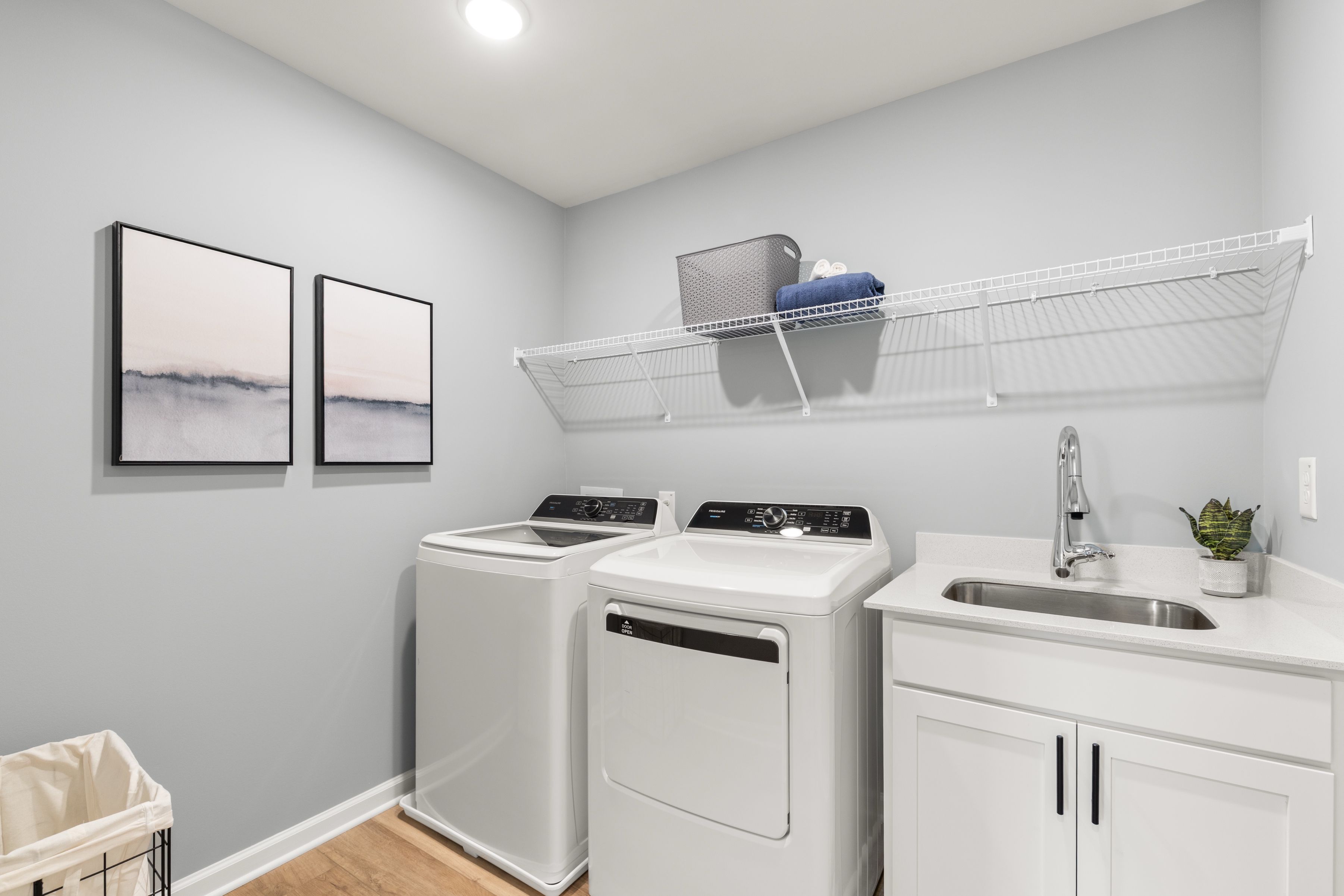 Spacious laundry room at The Bluffs in Canton, Georgia by Davidson Homes with white washers, dryers, utility sink, wire shelving, and abstract wall art