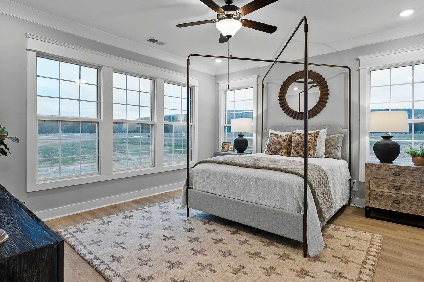 Spacious master bedroom in The Oxford featuring canopy bed, large windows, neutral gray walls, and farmhouse accents
