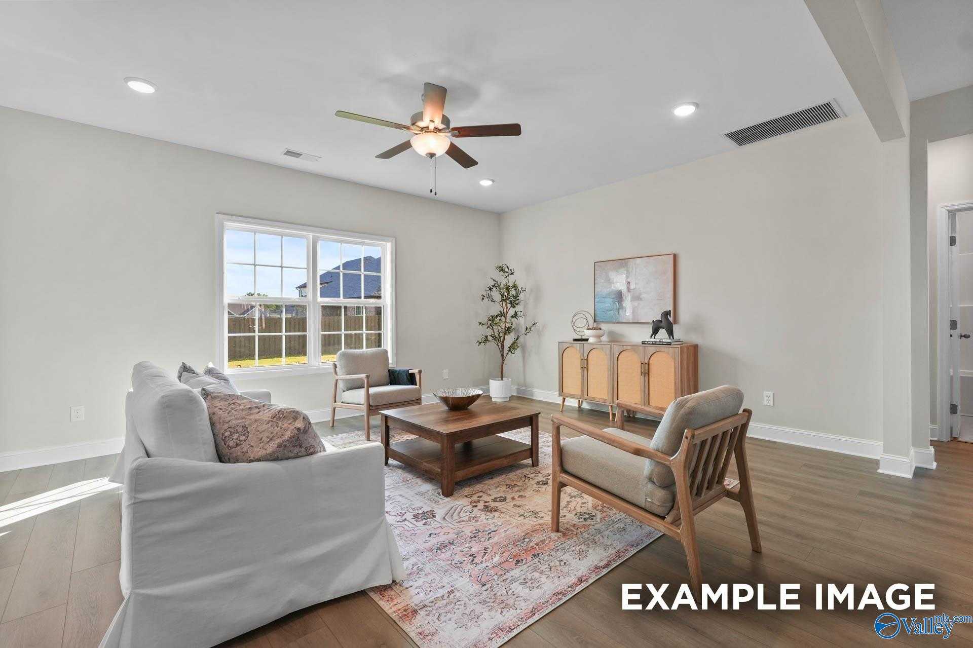 Cozy living room with beige sofa, wooden coffee table, accent chair, and large windows in Davidson Homes The Madison A, Harvest, Alabama