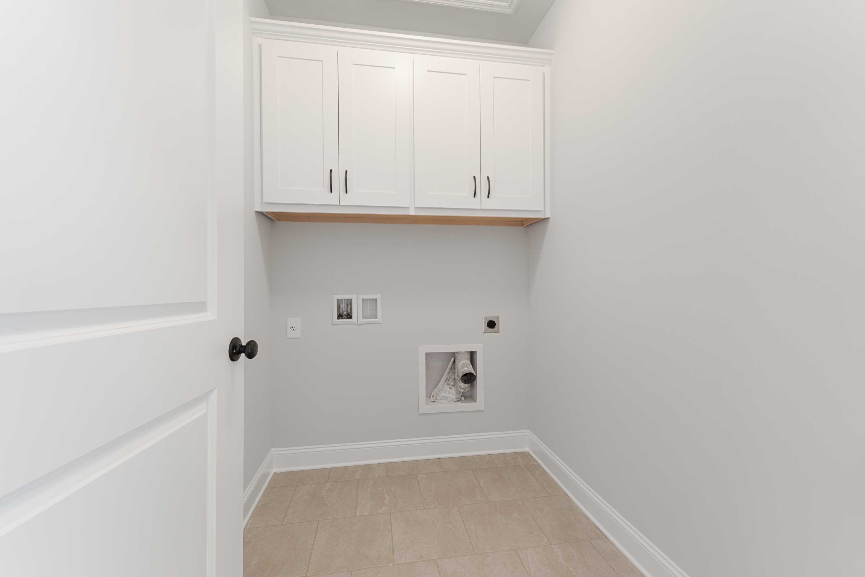 Spacious laundry room in The Copeland home design with white upper cabinets, utility sink, gray walls, and tiled floor