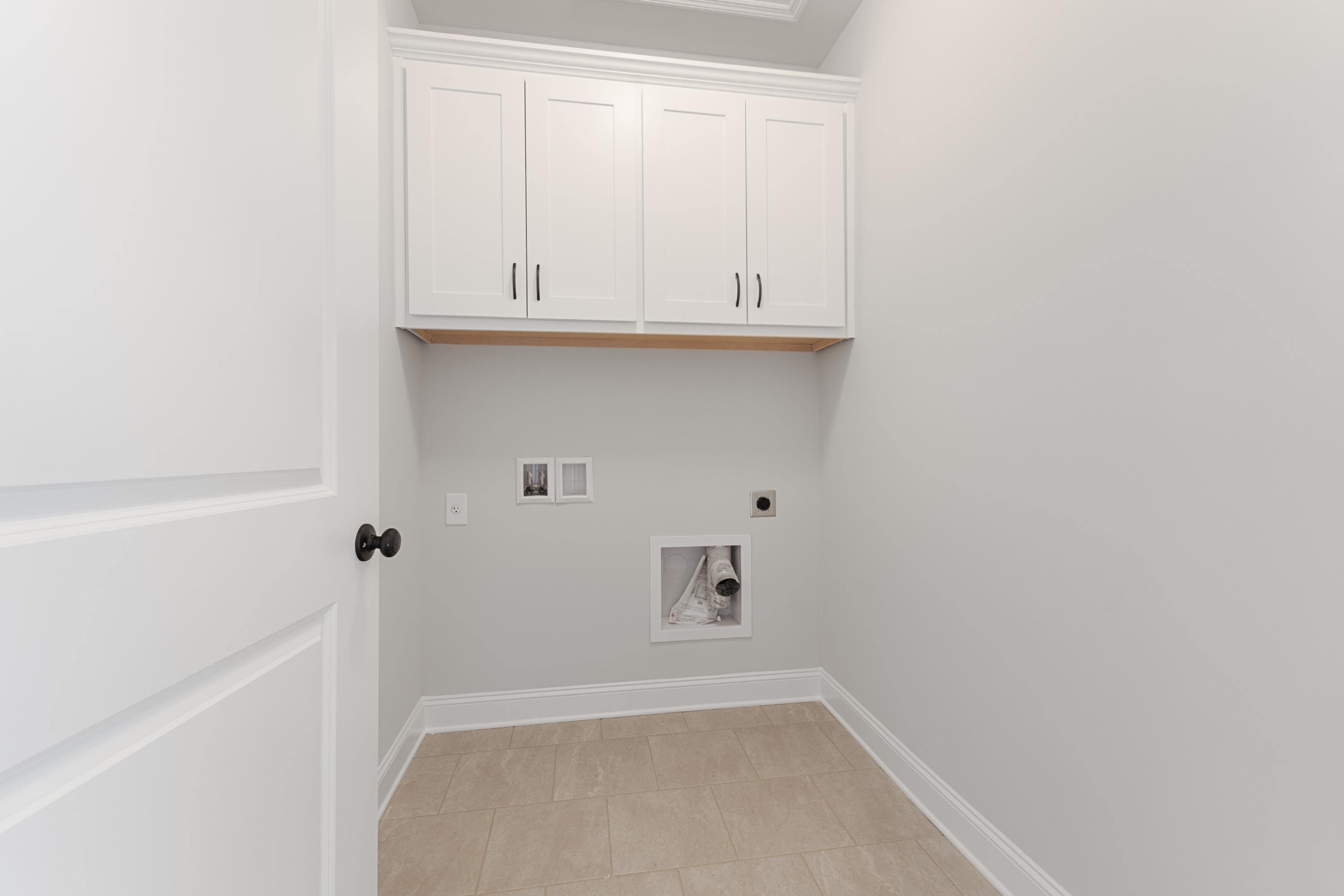 Spacious laundry room in The Copeland with white upper cabinets, washer dryer hookups, and light gray walls