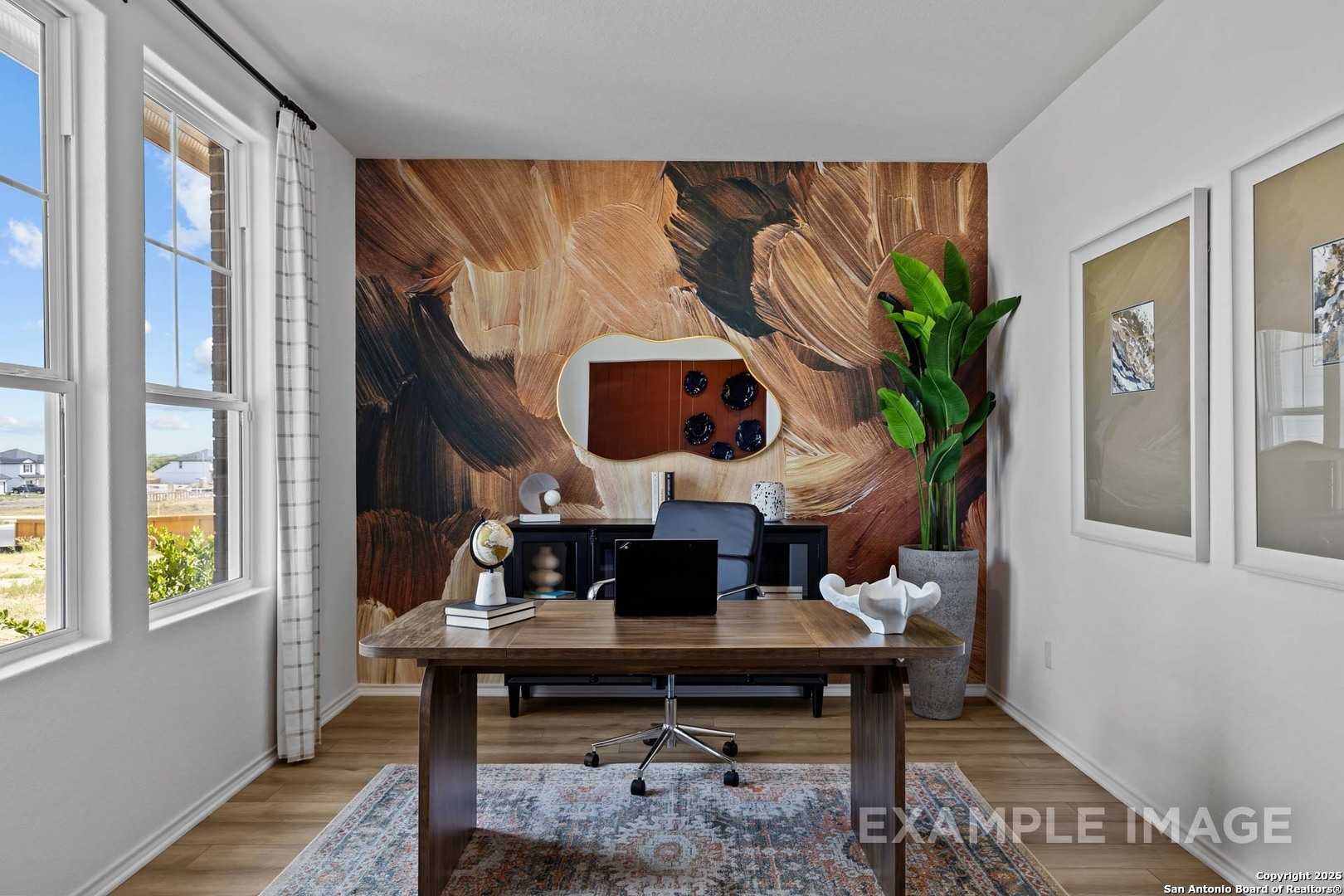 Modern home office with earthy abstract mural, wooden desk setup, potted plant, and window views in The Douglas C, Seguin, Texas