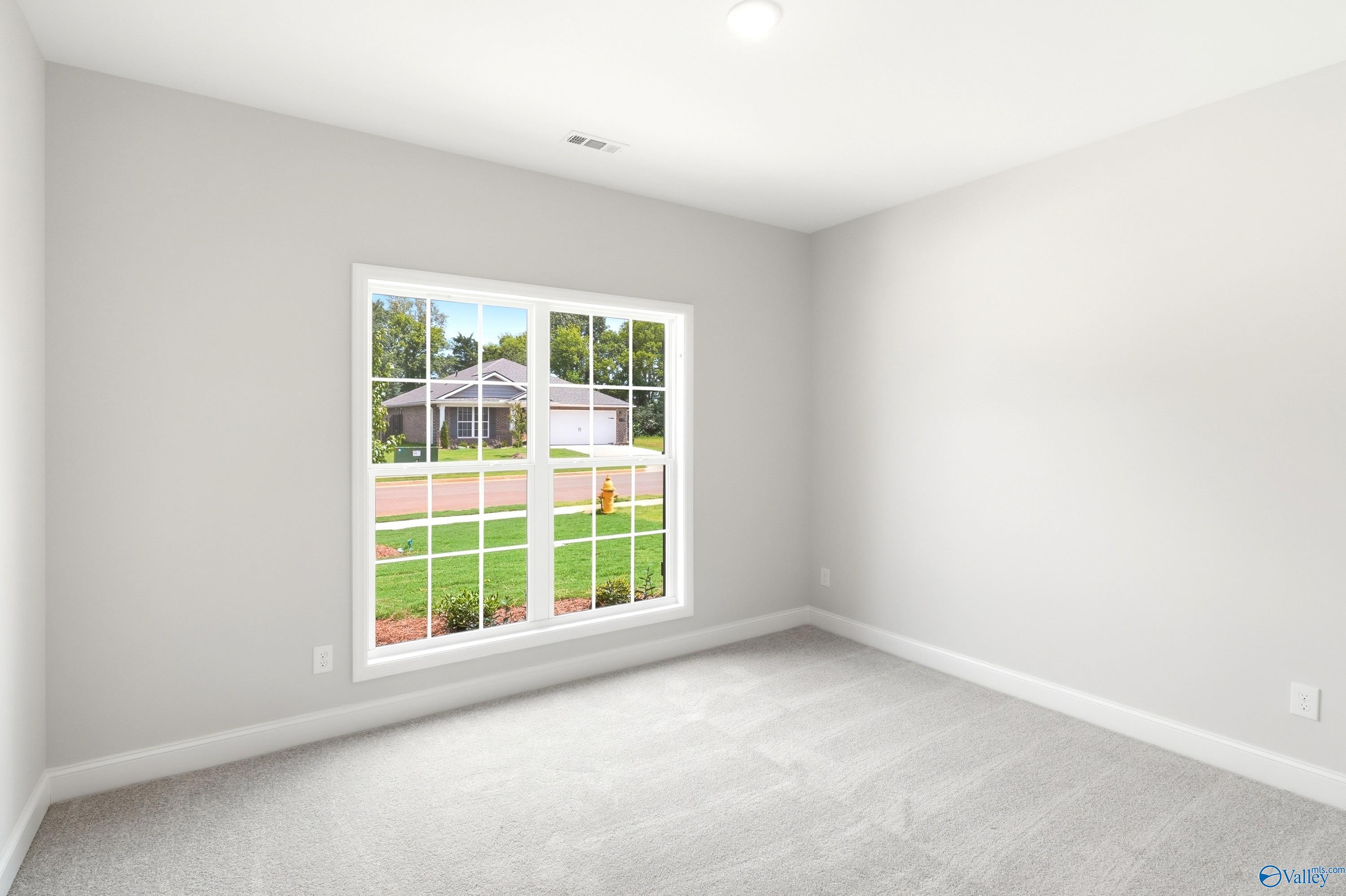 Bright, carpeted bedroom with large window in The Daphne floor plan by Davidson Homes in Lynn Meadows, Meridianville, AL.