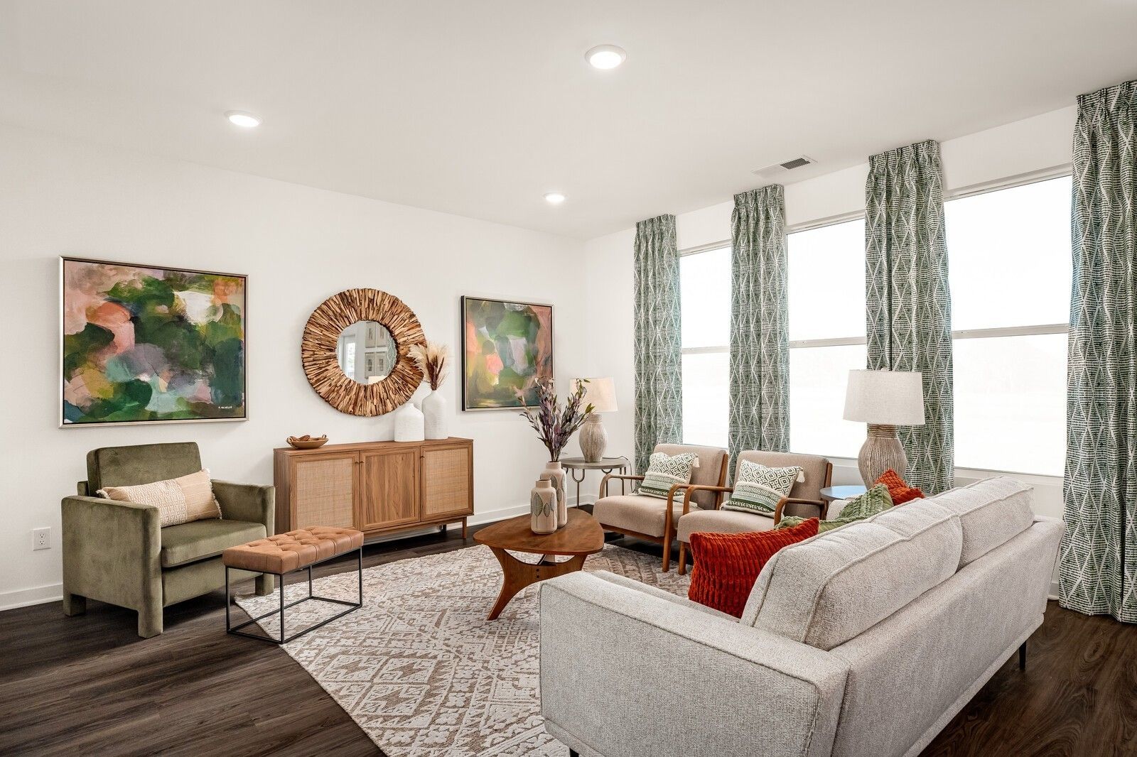 Cozy modern living room with gray sofa, green velvet armchair, abstract art, rattan mirror, and large windows in Davidson Homes The Gordon C, White House, TN