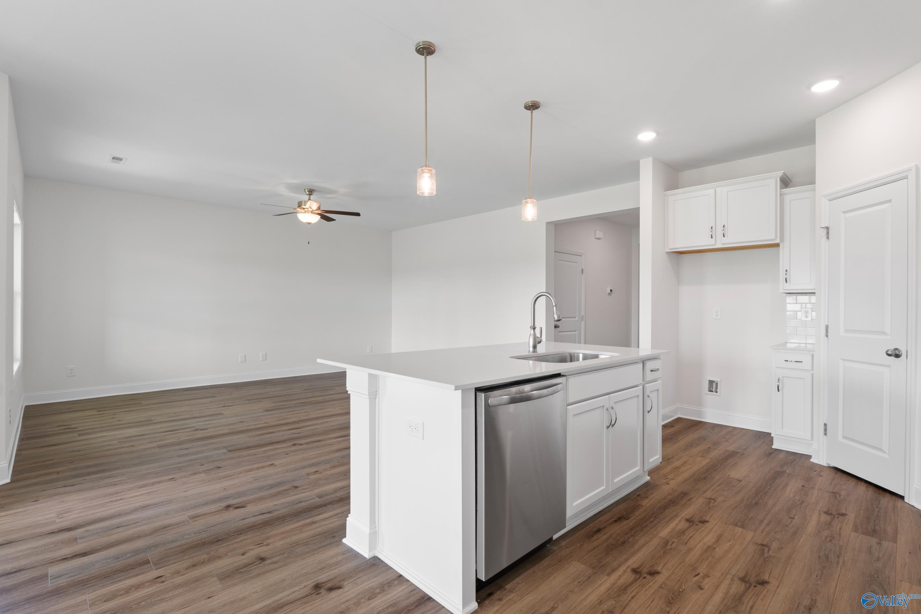 Open-concept kitchen with white cabinets, island, and wood-look flooring in The Everett B home at The Meadows in Athens, AL.