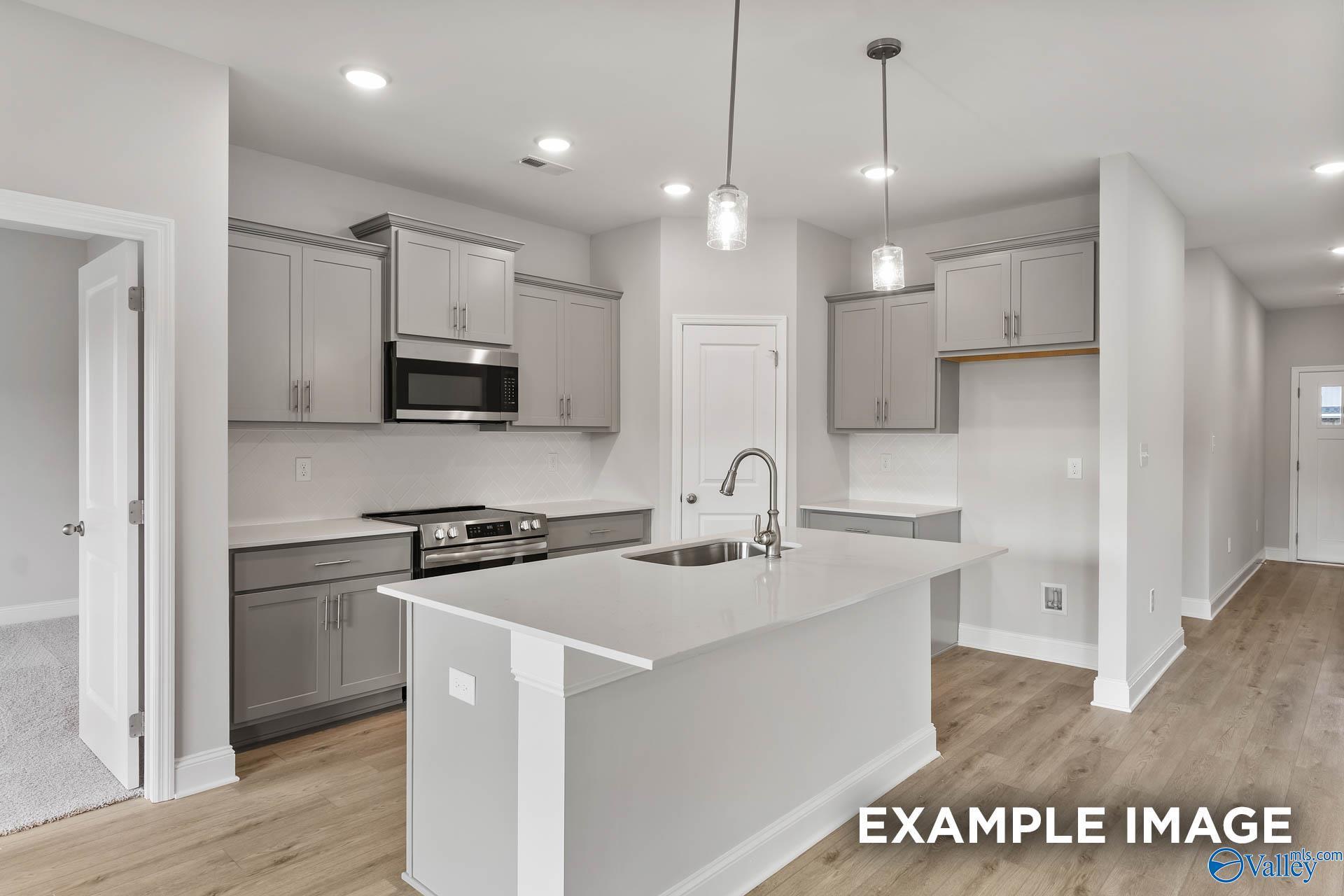 Modern open-concept kitchen with gray cabinets, white island sink, stainless appliances in Davidson Homes The Franklin, Athens AL