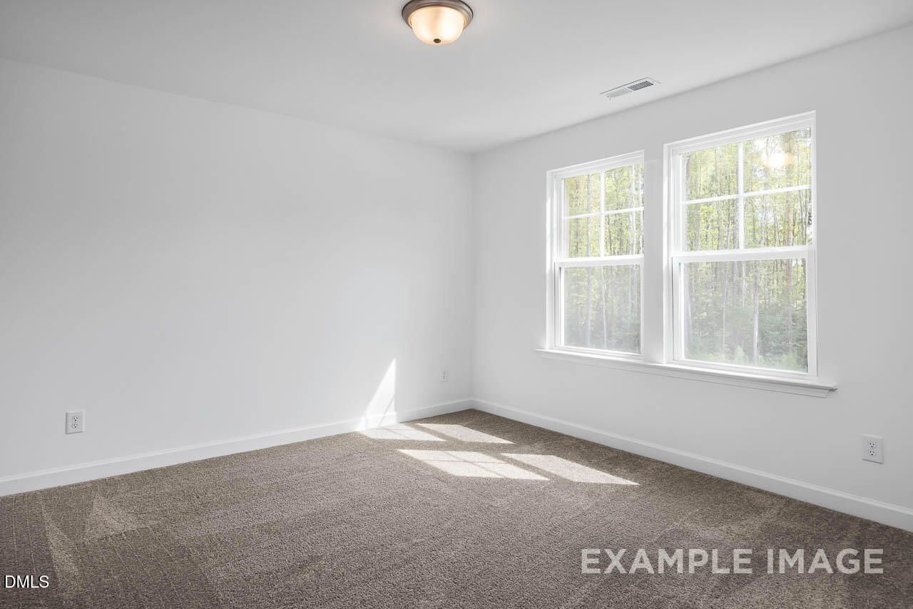 Bright empty bedroom with large windows, natural light, and beige carpet in Davidson Homes The Willow D, Zebulon, NC