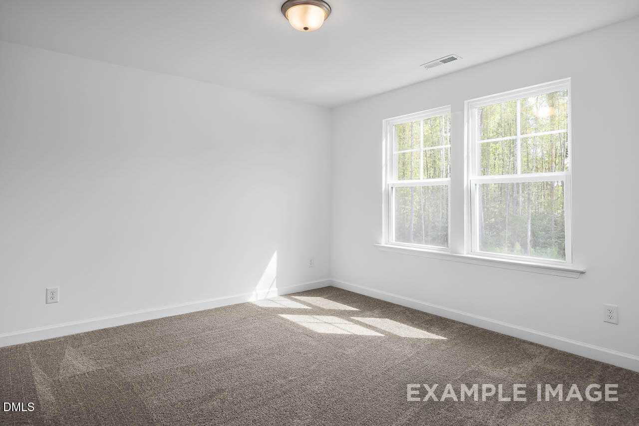 Bright empty bedroom with large windows, natural light, and beige carpet in Davidson Homes The Willow D, Zebulon, NC