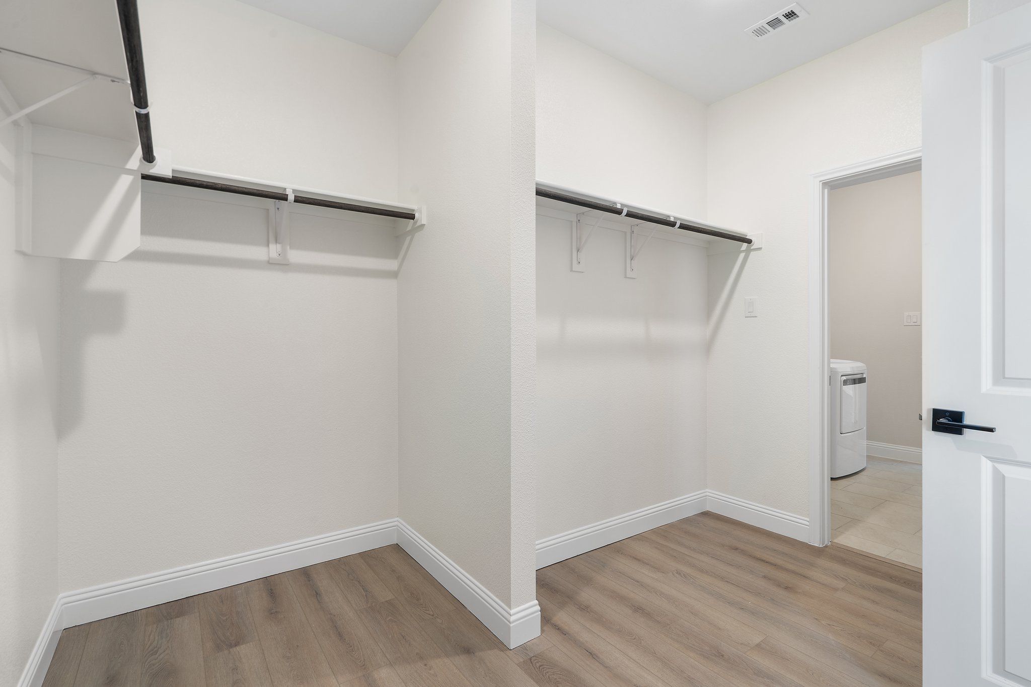 Spacious walk-in closet in The Holly F master suite featuring built-in shelving, hanging rods, and direct laundry room access.