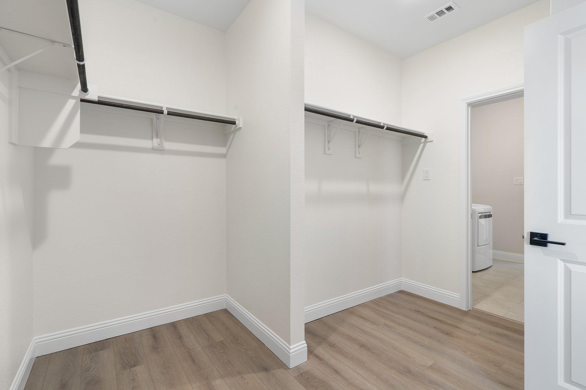 Spacious walk-in closet in The Holly F master suite featuring built-in shelving, hanging rods, and direct laundry room access.