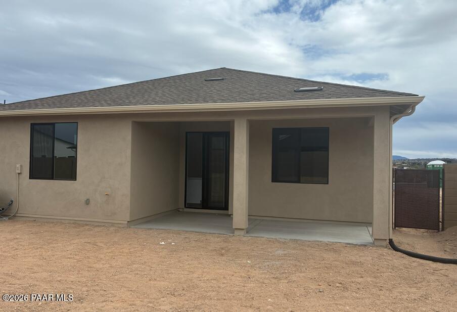 Rear view of beige stucco 1-story home with covered patio, sliding glass doors, and desert yard in Prescott, Arizona