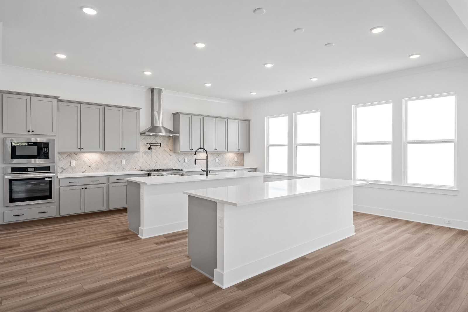 Modern kitchen with gray cabinets, white quartz islands, stainless appliances, and large windows in The Alston A, Murfreesboro, TN