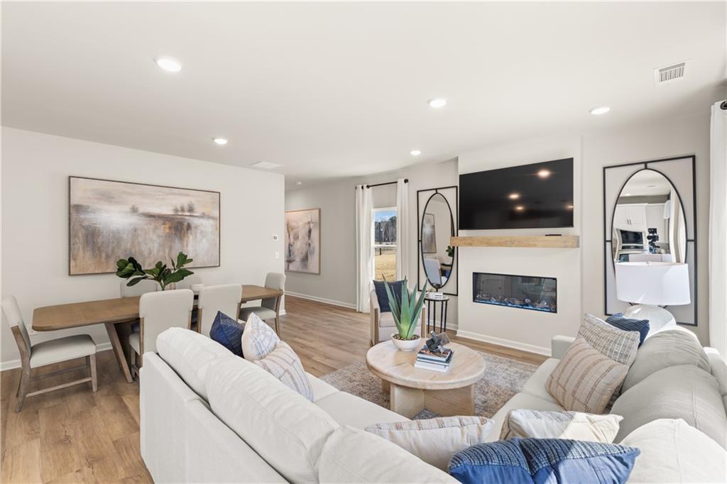 Cozy open living room with white sectional sofa, gas fireplace, TV, and dining table in Davidson Homes The Burton C, Canton, Georgia