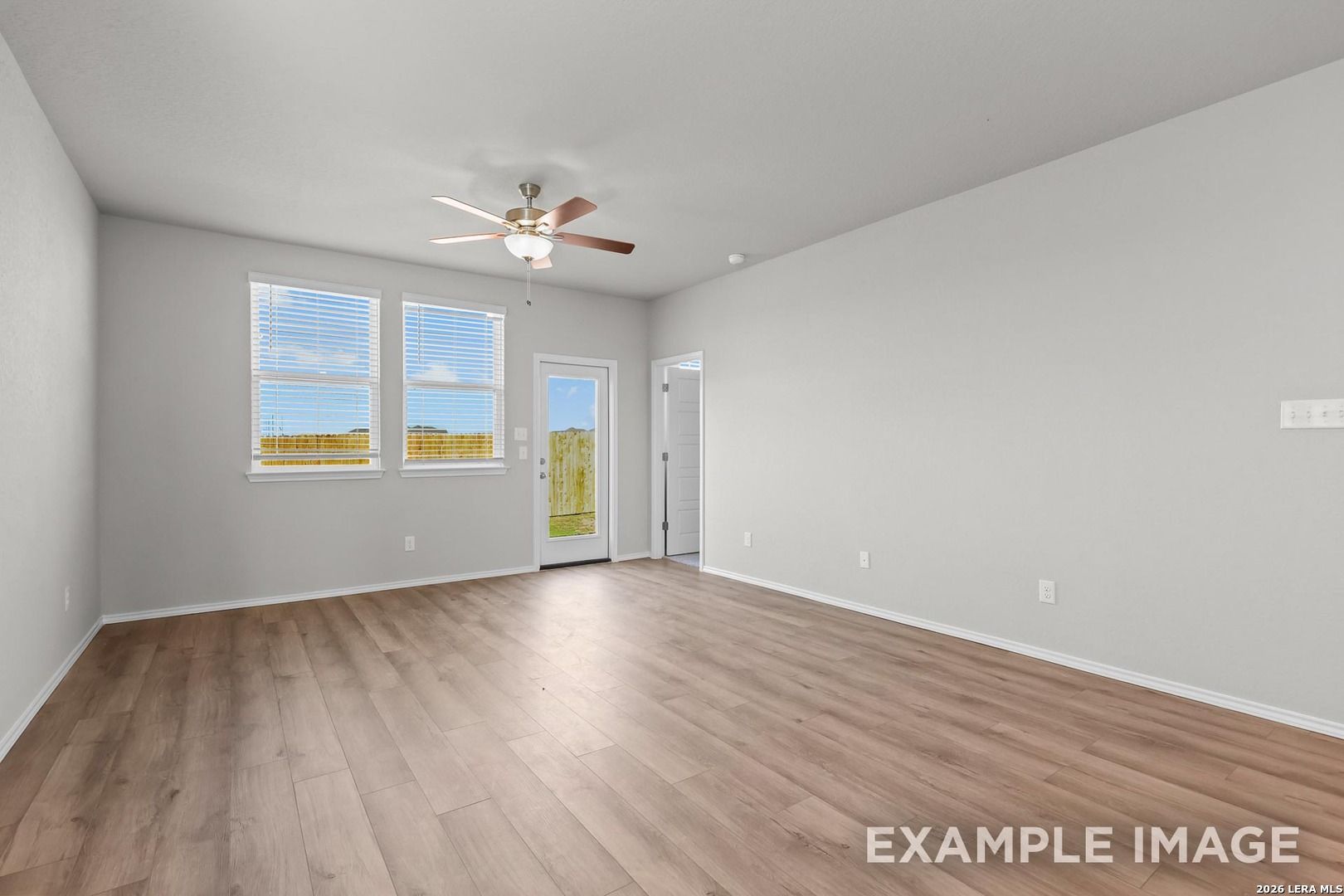 Bright living room with light hardwood floors, ceiling fan, large windows, and French doors in 4-bedroom Davidson Homes The Colorado D, Agave, San Antonio, Texas