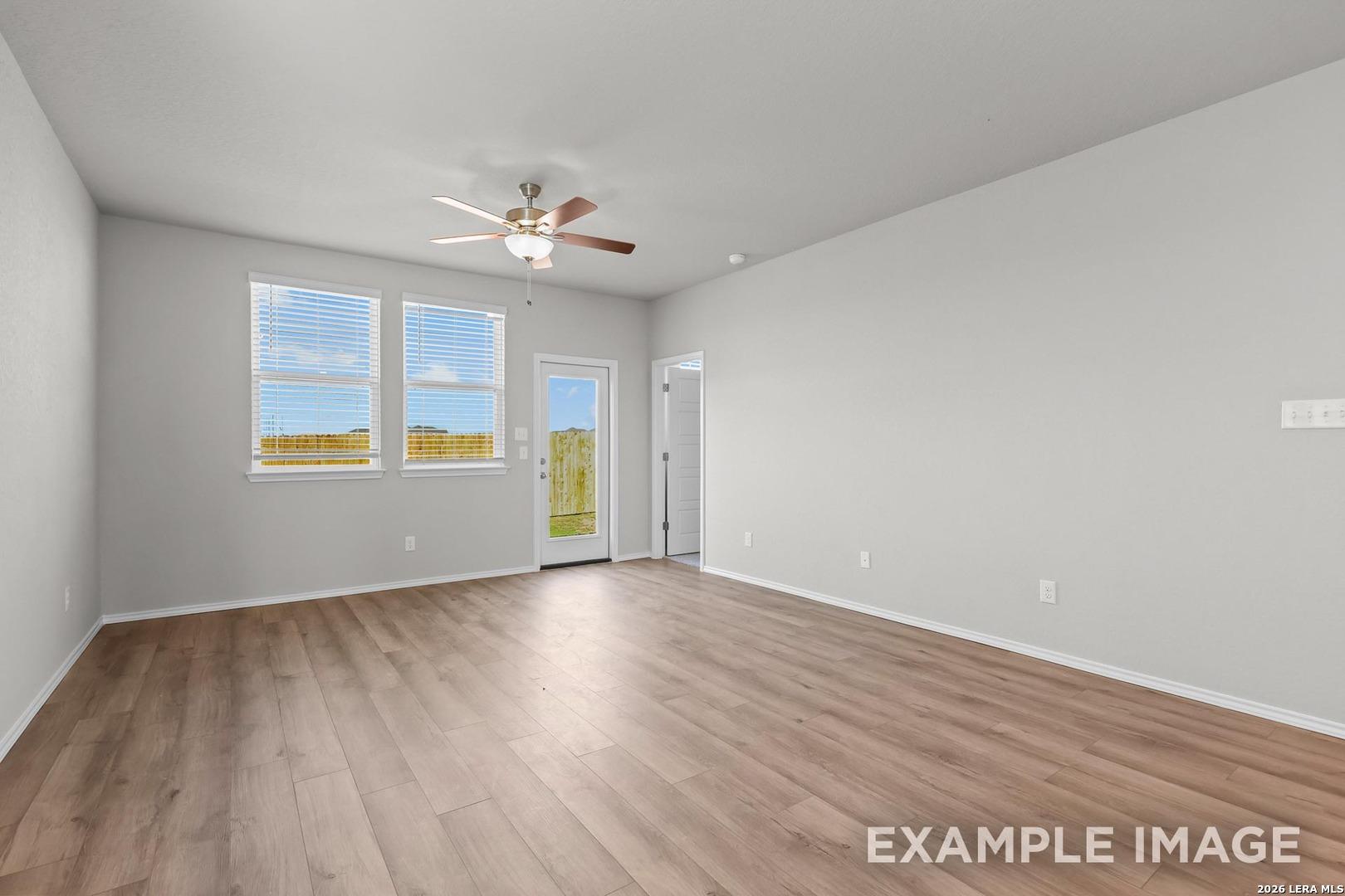 Bright living room with light hardwood floors, ceiling fan, large windows, and French doors in 4-bedroom Davidson Homes The Colorado D, Agave, San Antonio, Texas