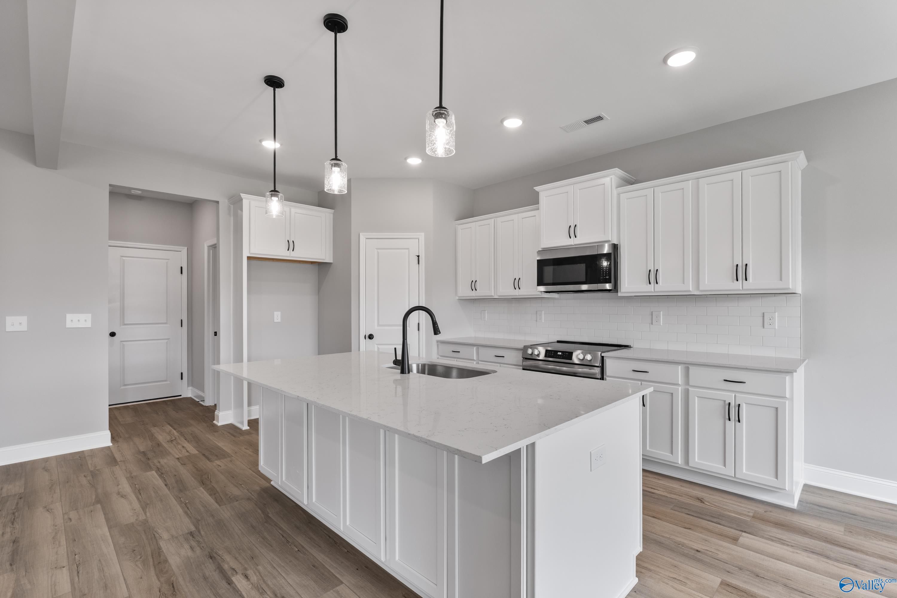 Modern white kitchen with quartz island, stainless microwave, pendant lights, and hardwood floors in Davidson Homes Montgomery B, Toney, AL