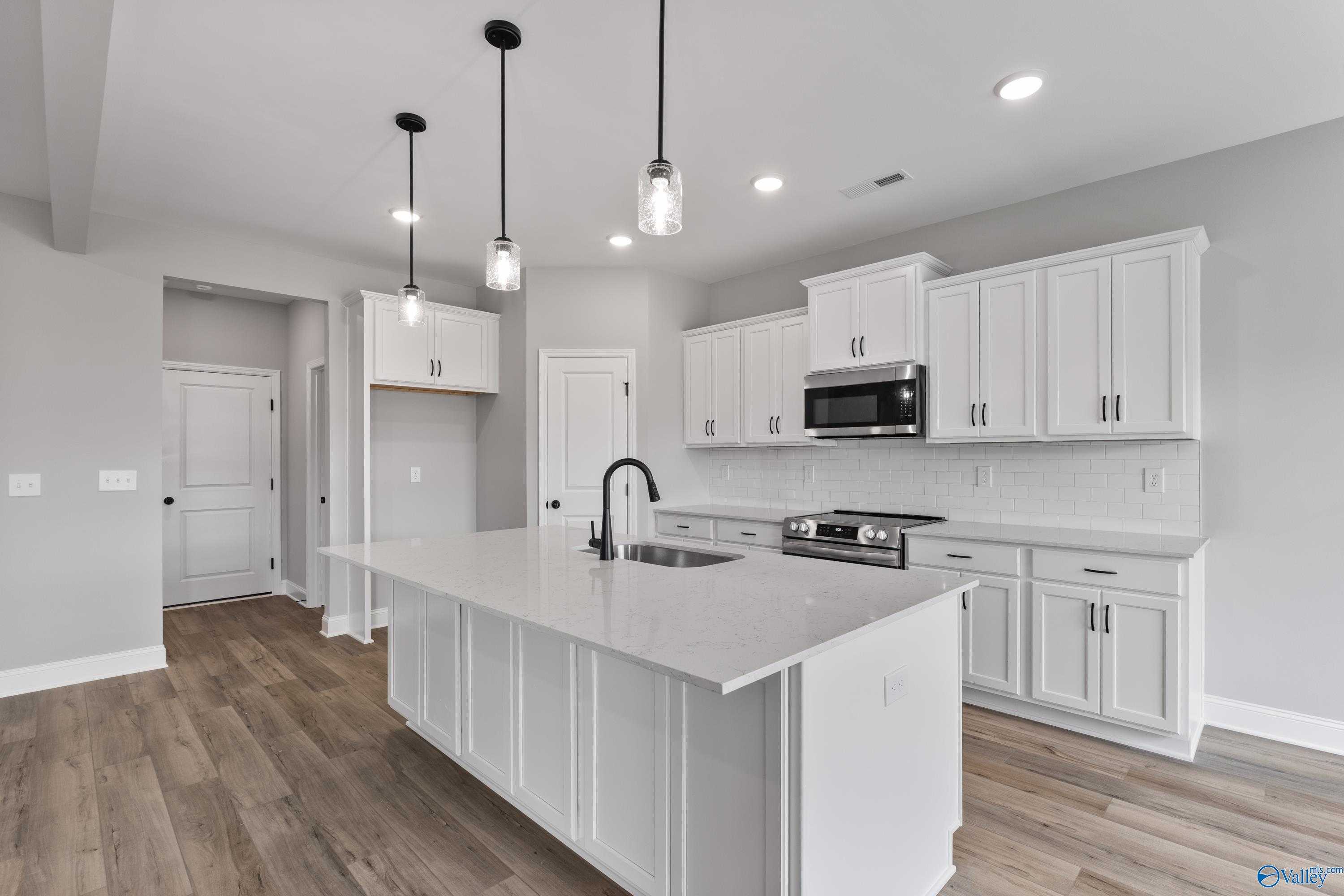 Modern white kitchen island with quartz countertop, stainless microwave, and pendant lights in Davidson Homes Montgomery B, Toney, AL