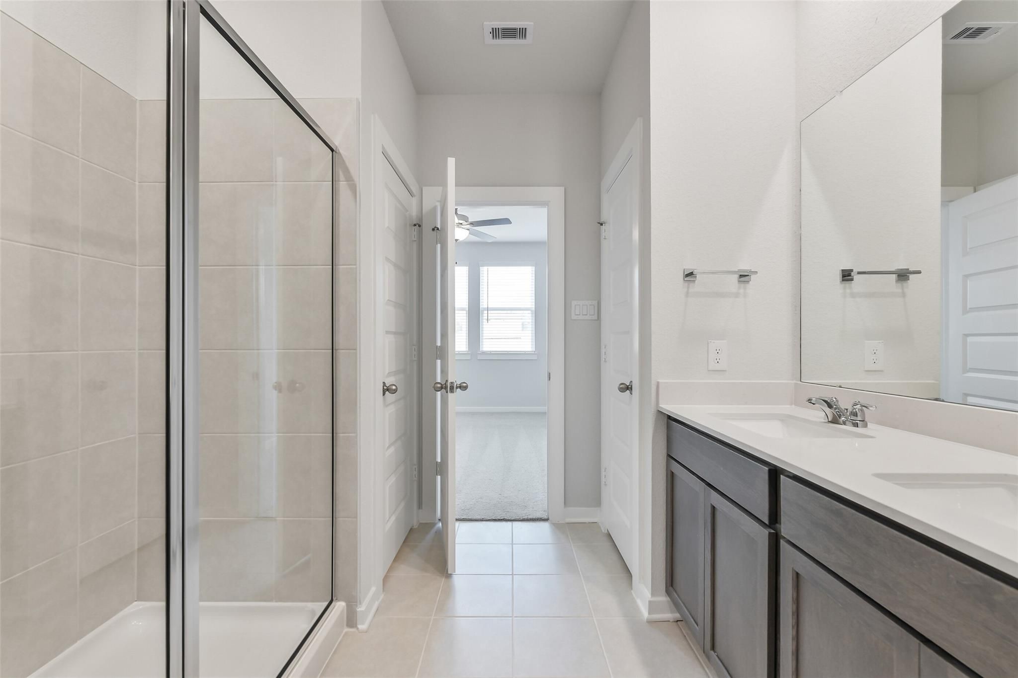 Modern master bathroom with glass shower enclosure, double vanity, and tile floor in Davidson Homes The Brazos E, Cleveland, Texas